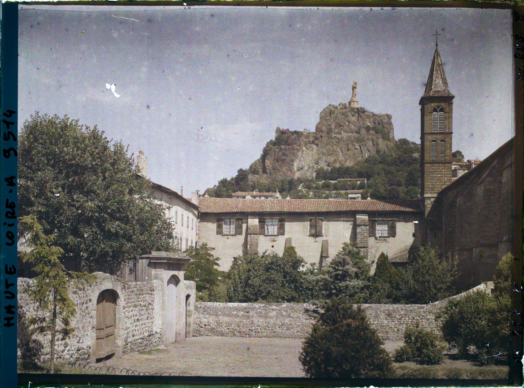 Image représentant L'orphelinat et le clocher de l'église Saint-Laurent avec à l'arrière-plan, le rocher de la Vierge avec la statue de Notre-Dame-de-France