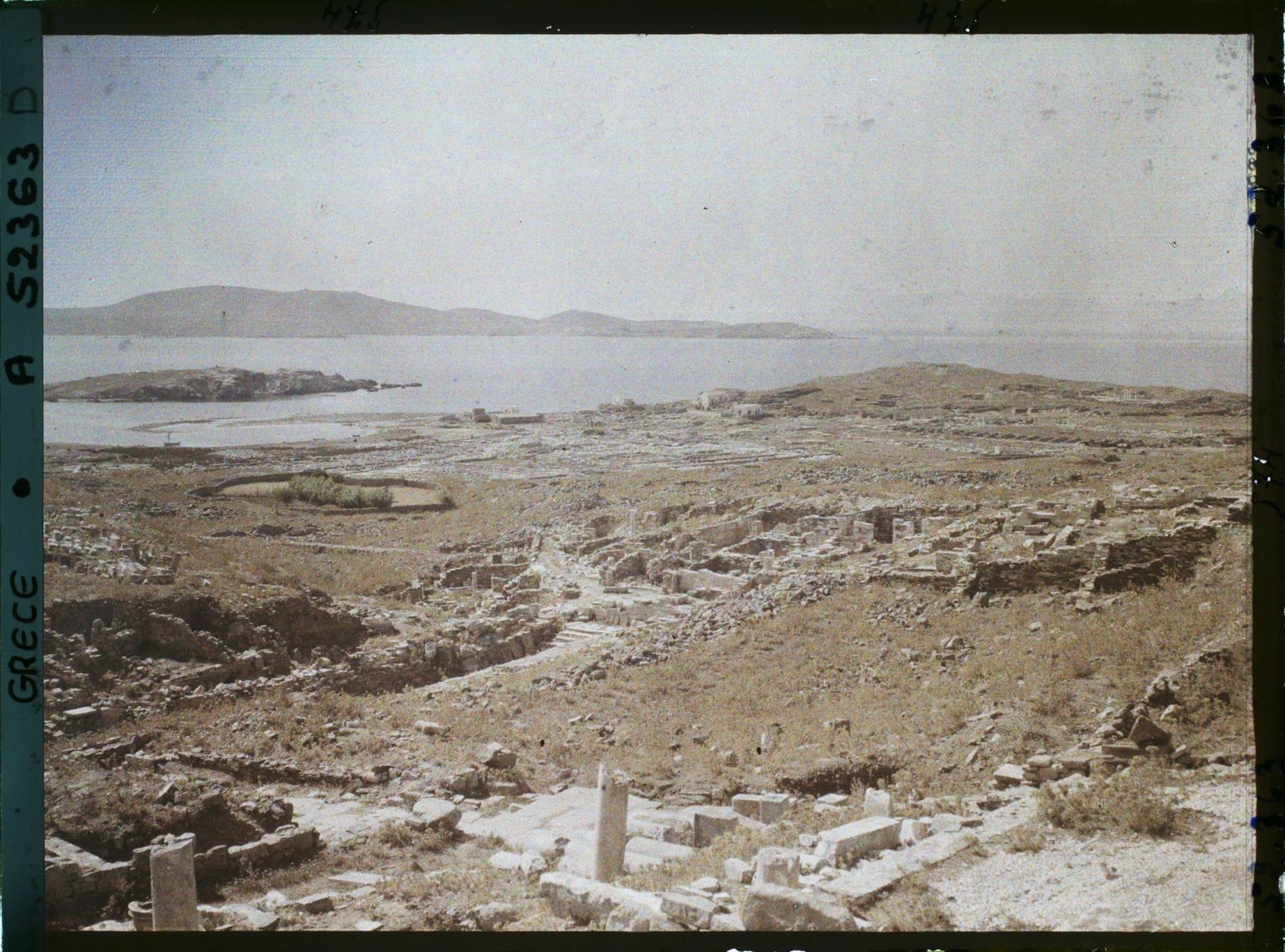 Image représentant Panorama sur les ruines de la ville antique (haute et basse) et la mer depuis la terrasse des Dieux étrangers sur le versant occidental du mont Cynthe (au fond, l'ile de Syros)