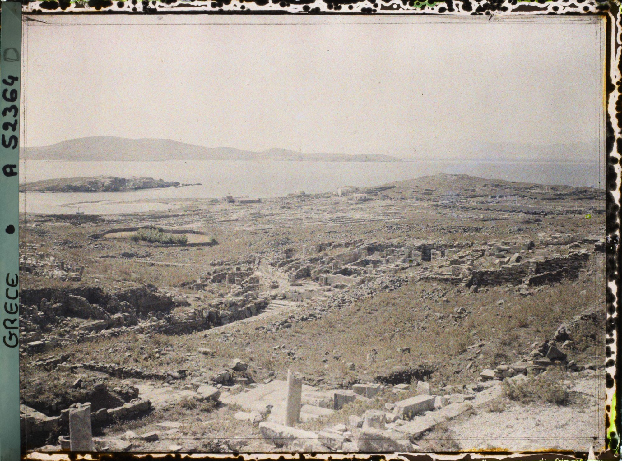 Image représentant Panorama sur les ruines de la ville antique (haute et basse) et la mer depuis la terrasse des Dieux étrangers sur le versant occidental du mont Cynthe (au fond, l'ile de Syros)