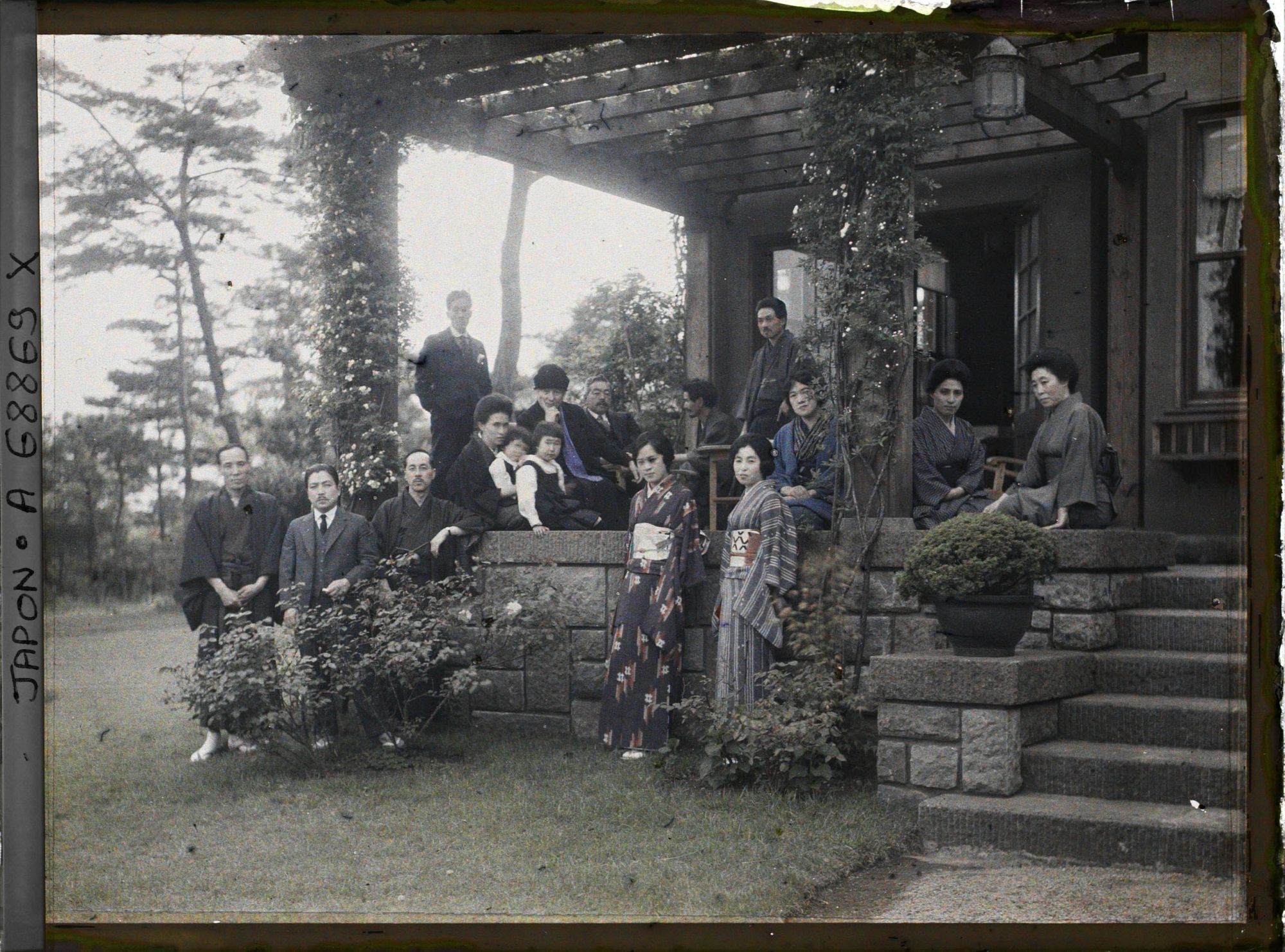 Image représentant groupe d'hommes, de femmes et d'enfants, les uns en tenue traditionnelle, les autres vêtus à l'occidentale (les hommes surtout) sur une terrasse.