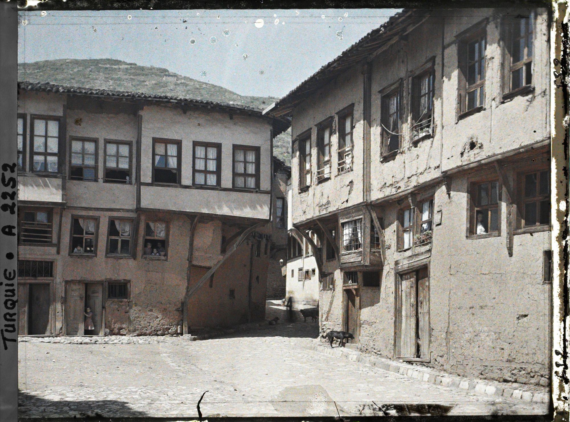 Image représentant Deux maisons presque identiques (l'une en bon état, l'autre moins) de part et d'autre d'une place pavée