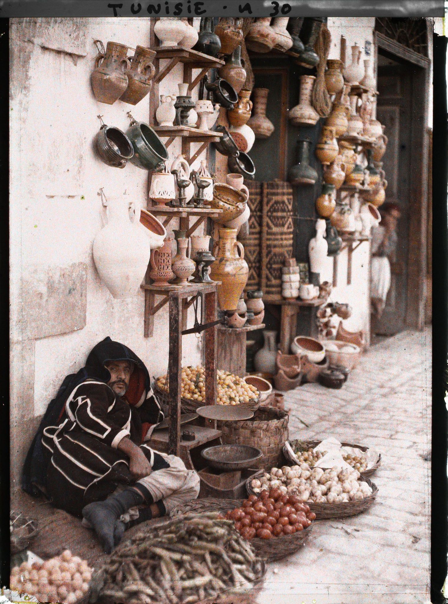 Image représentant Un marchand de fruits et légumes devant une boutique de poteries dans un souk de la médina