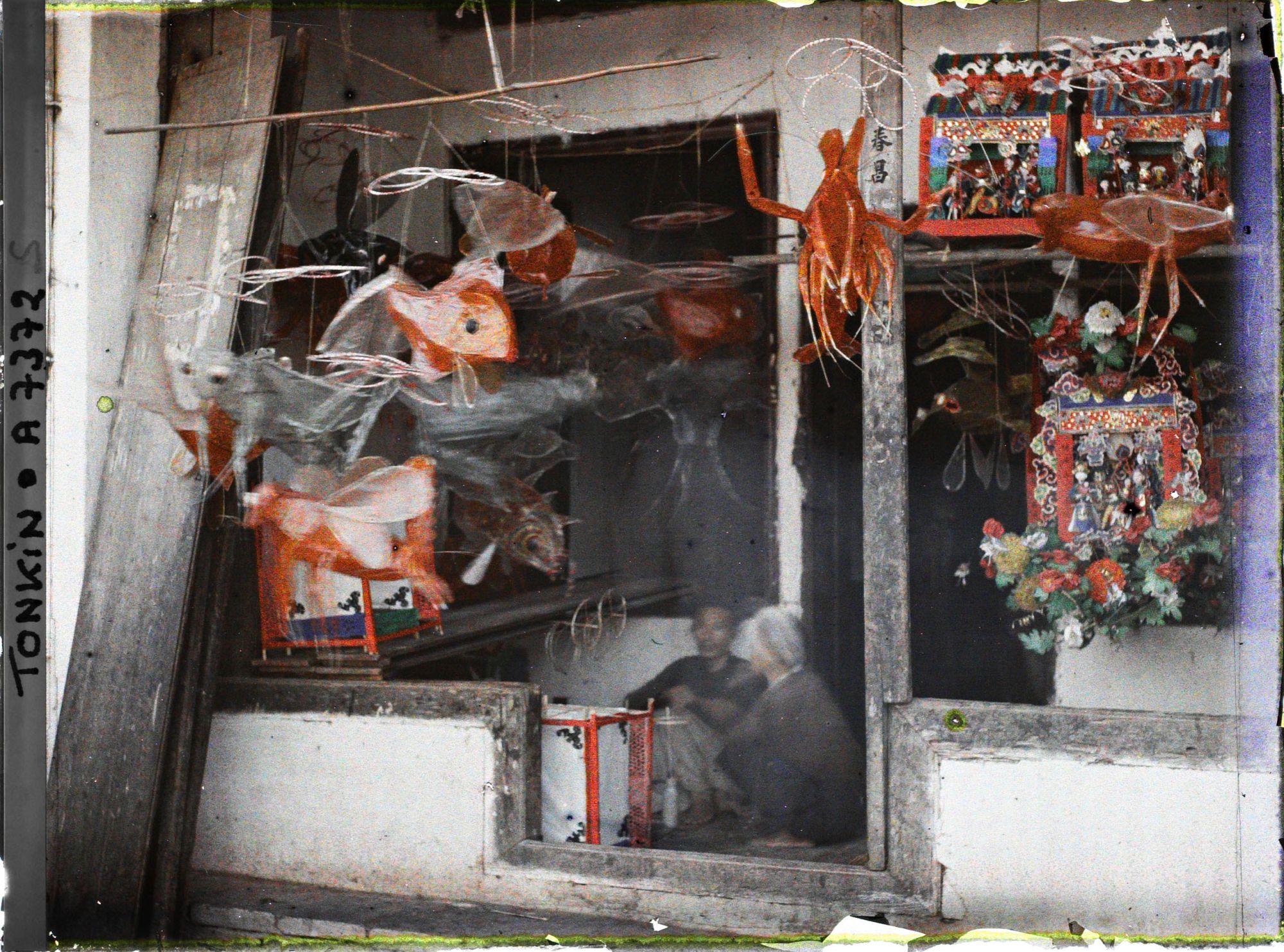 Image représentant Un étalage de jouets en papier huilé devant une boutique, dans la " rue du Chanvre "