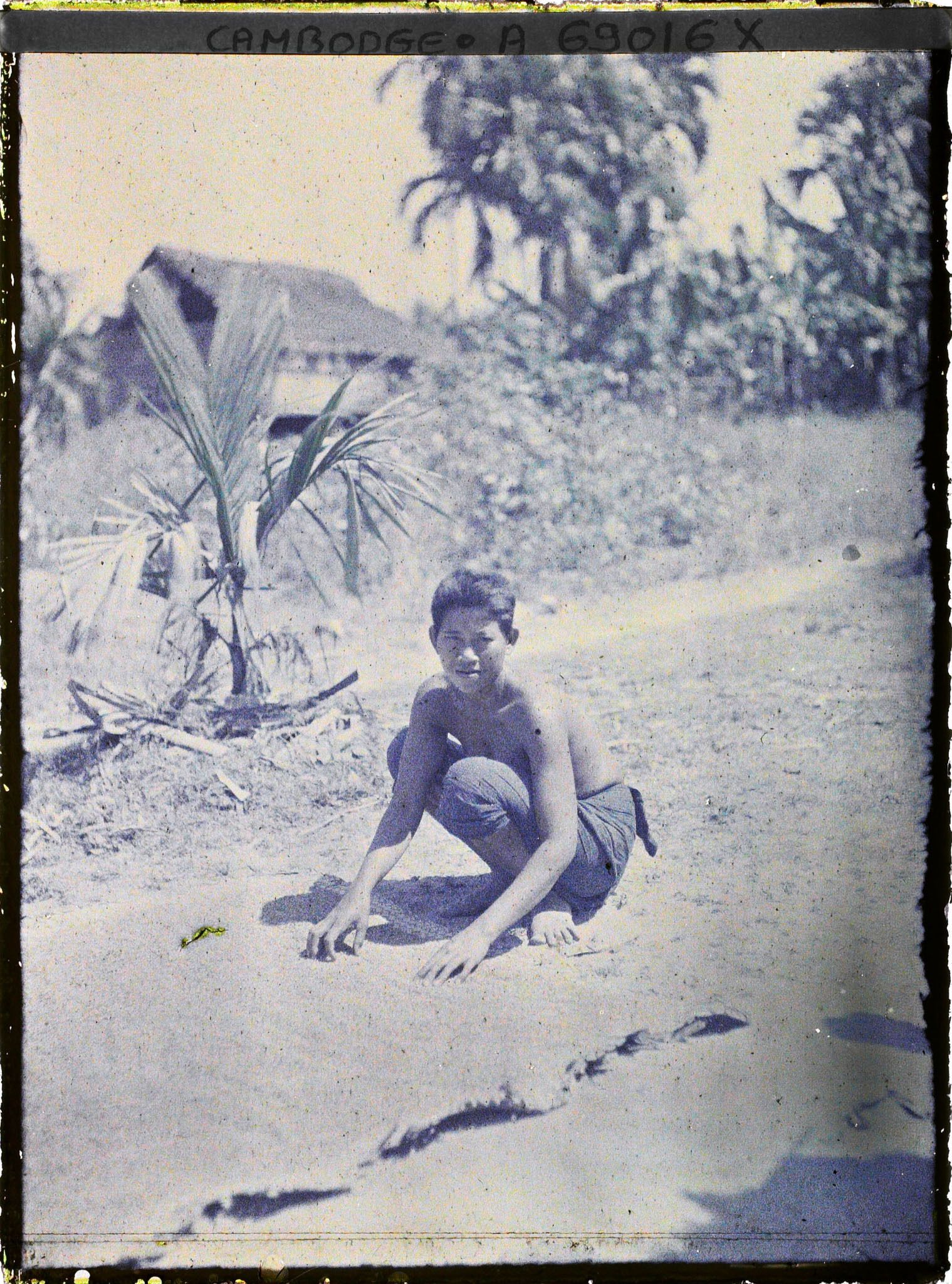 Image représentant Une jeune femme en sampot, torse nu, accroupie près d&#039;une natte