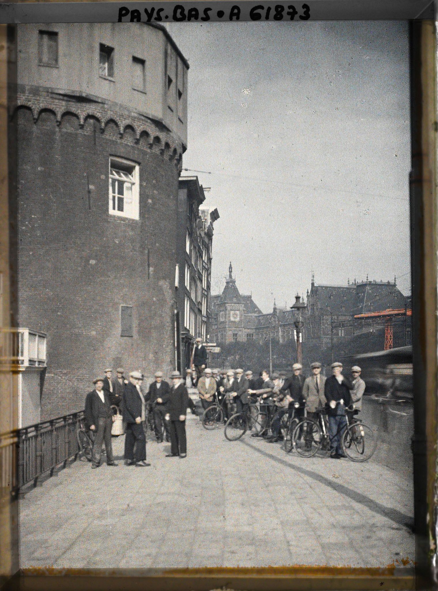Image représentant Un groupe sur le Prins Hendrik Kade, près du Schreierstoren, avec la gare centrale à l'arrière-plan