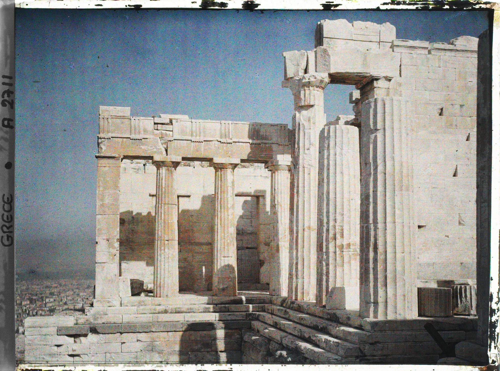 Image représentant Sur l'Acropole, la Pinacothèque (à l'arrière plan) et les Propylées de Mnesicles (au premier plan). Au loin, la ville.