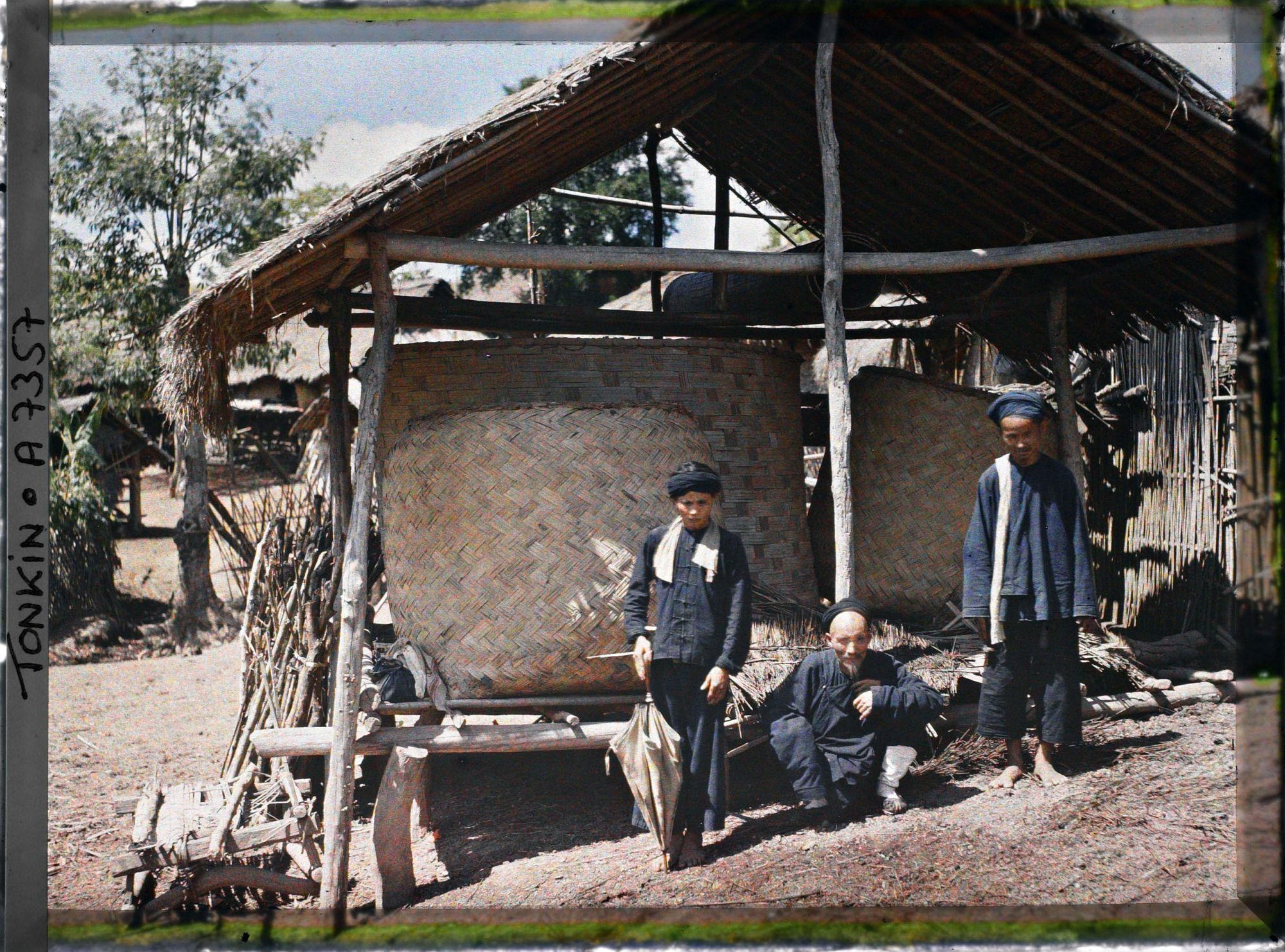 Image représentant Des villageois thô (thai), vêtus de bleu, devant un grenier à paddy