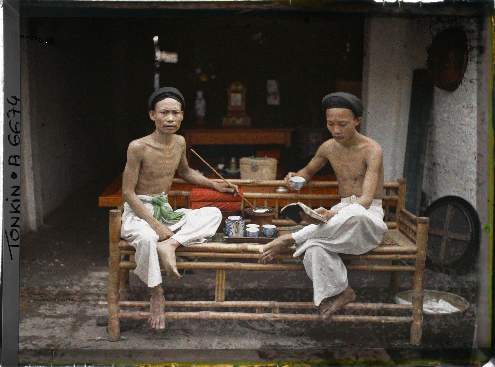 Image représentant Deux hommes prenant le thé, fumant la pipe à eau et lisant, assis sur une banquette en bambou