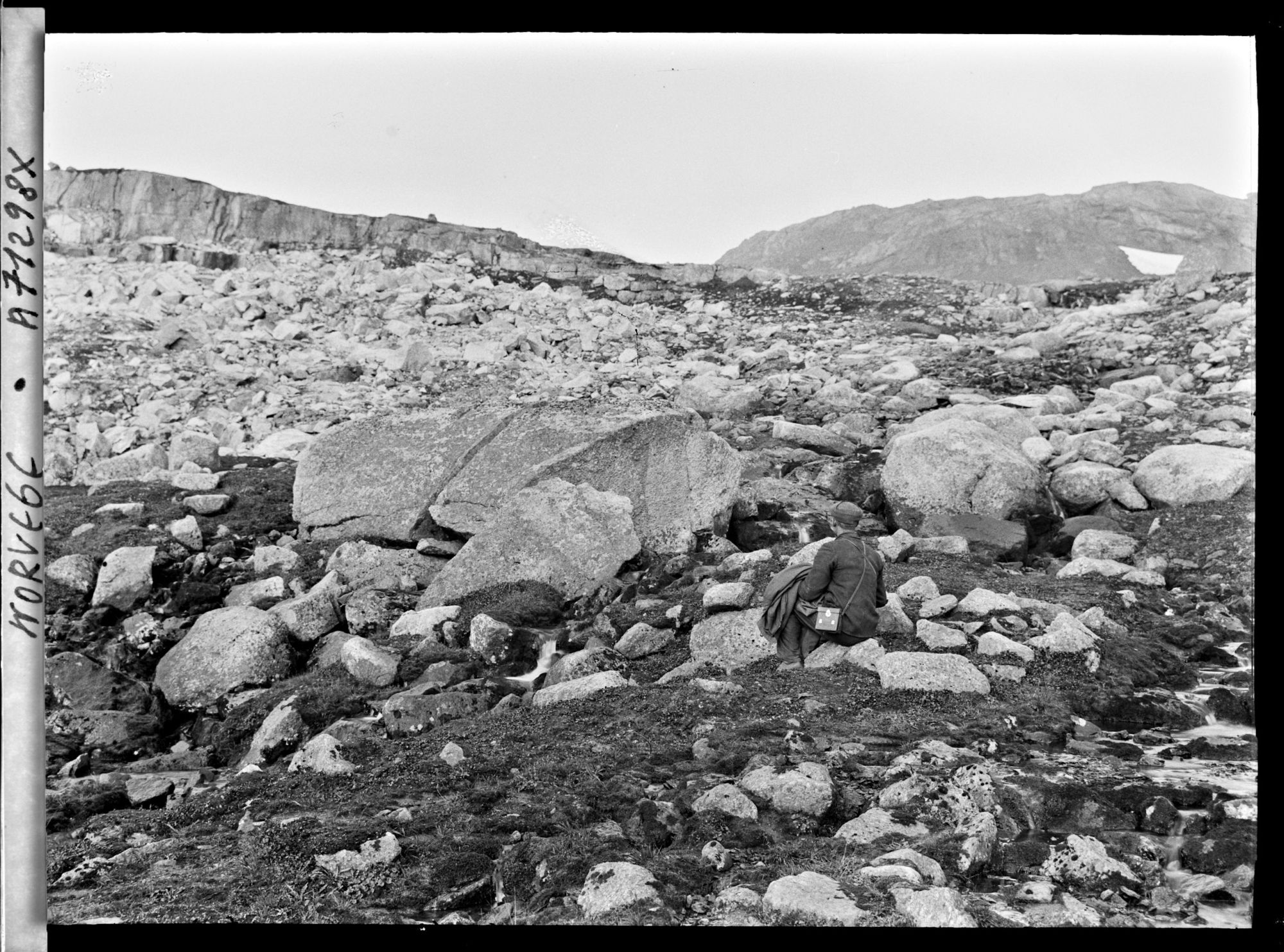 Image représentant L'assistant d'Anders Beer Wilse assis dans les éboulis à proximité du glacier Hardangerjökulen