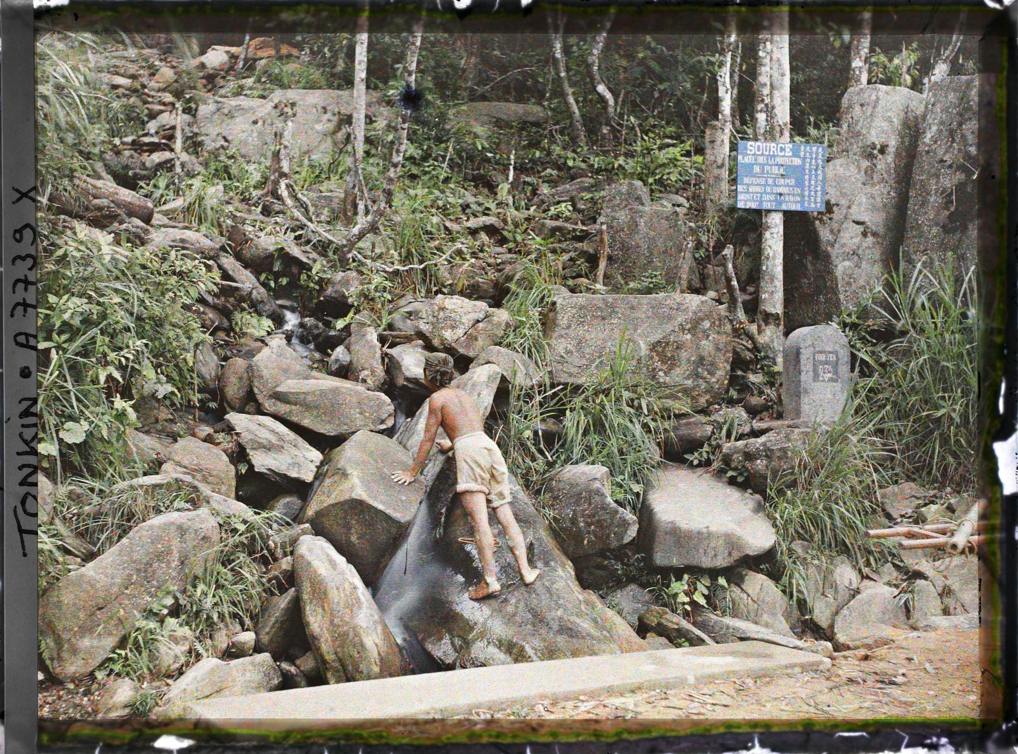 Image représentant Un homme, de dos, appuyé aux rochers à la source d'un petit cours d'eau, au bord de la route gravissant le massif du Tam-dao (" Trois Sommets ")