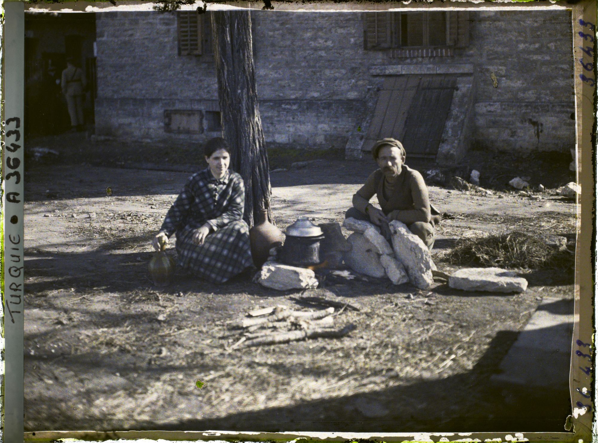Image représentant Un homme et une jeune femme grecs s'apprêtant à quitter la ville prêt d'un foyer improvisé