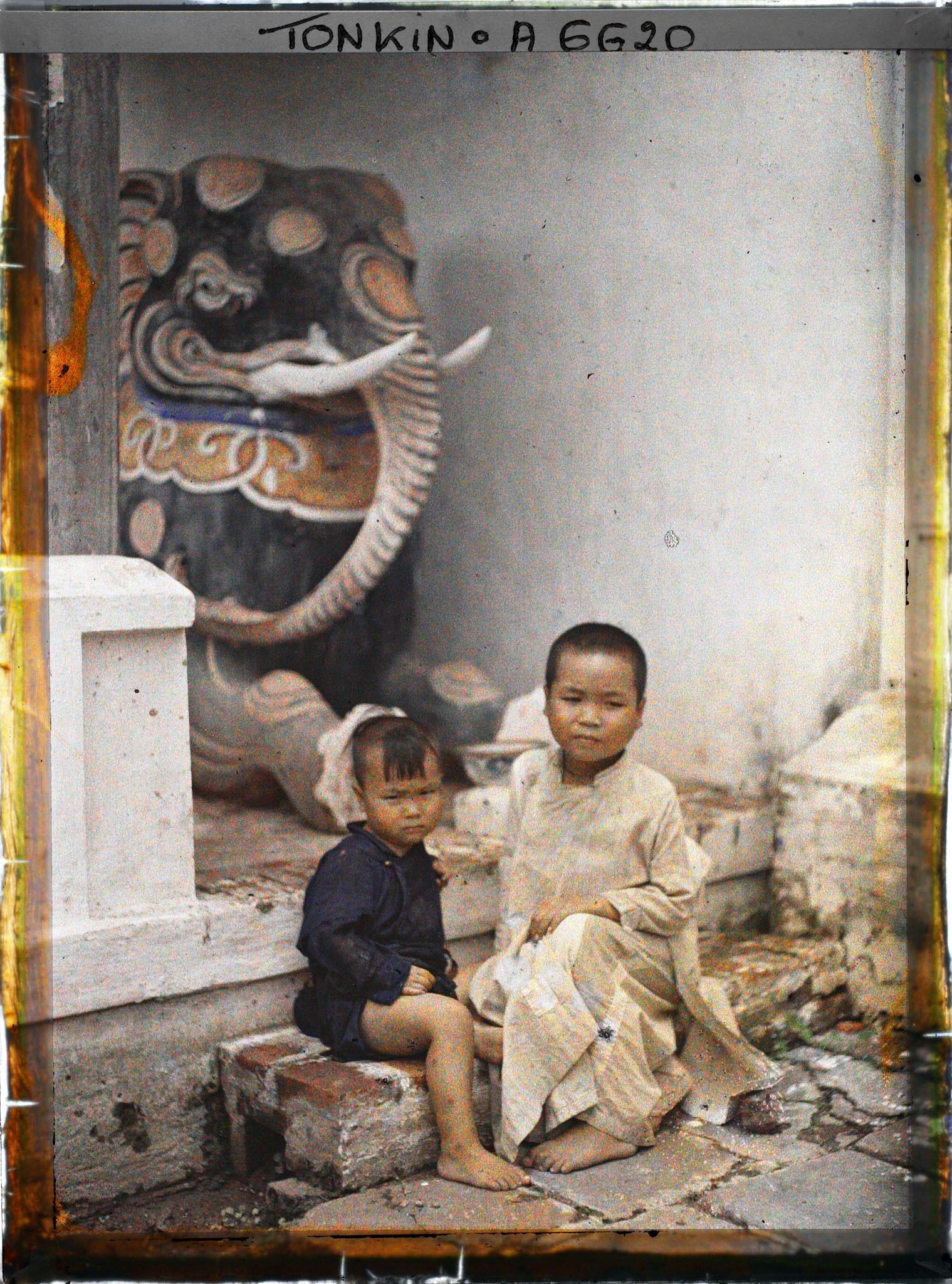 Image représentant Deux enfants assis devant une statue représentant un éléphant, à l'entrée du temple du village de Vinh-thuy