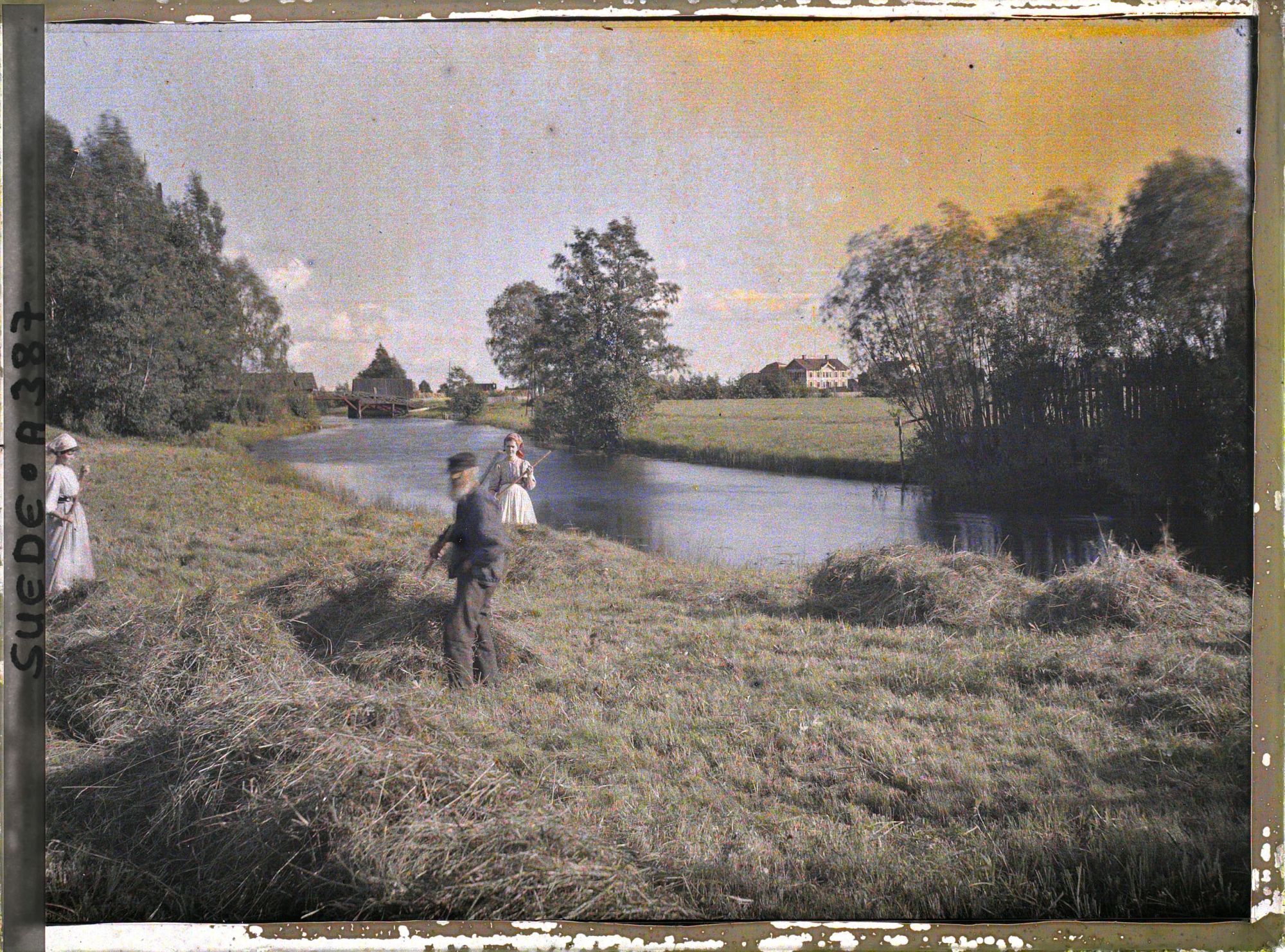 Image représentant Un homme et deux femmes fanant au bord d'une rivière (Alsjöbäcken ou Bansjän)