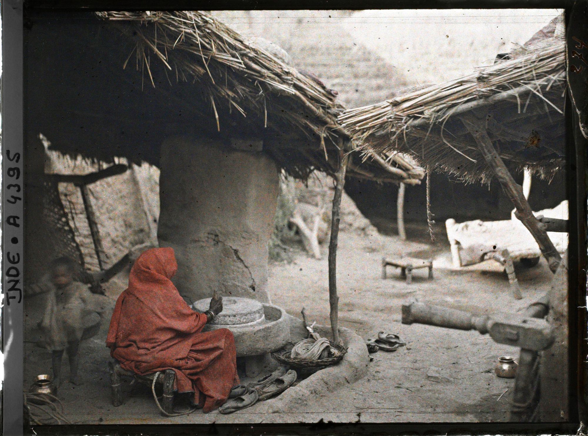 Image représentant Une femme actionnant une meule à farine sous l'auvent d'une maison