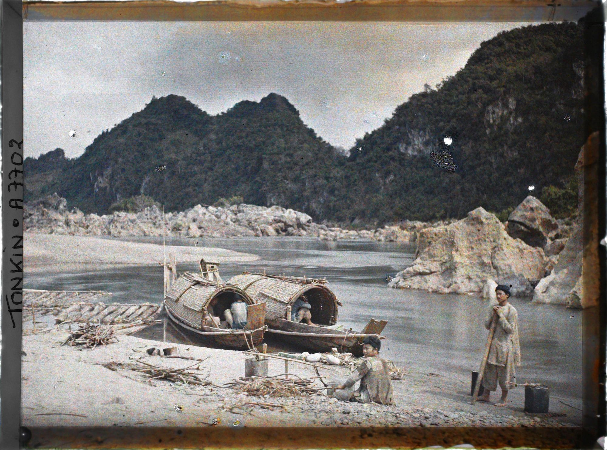 Image représentant Des Mnongs et des sampans, amarés juste en aval du barrage de rochers entravant le cours de la rivière Noire