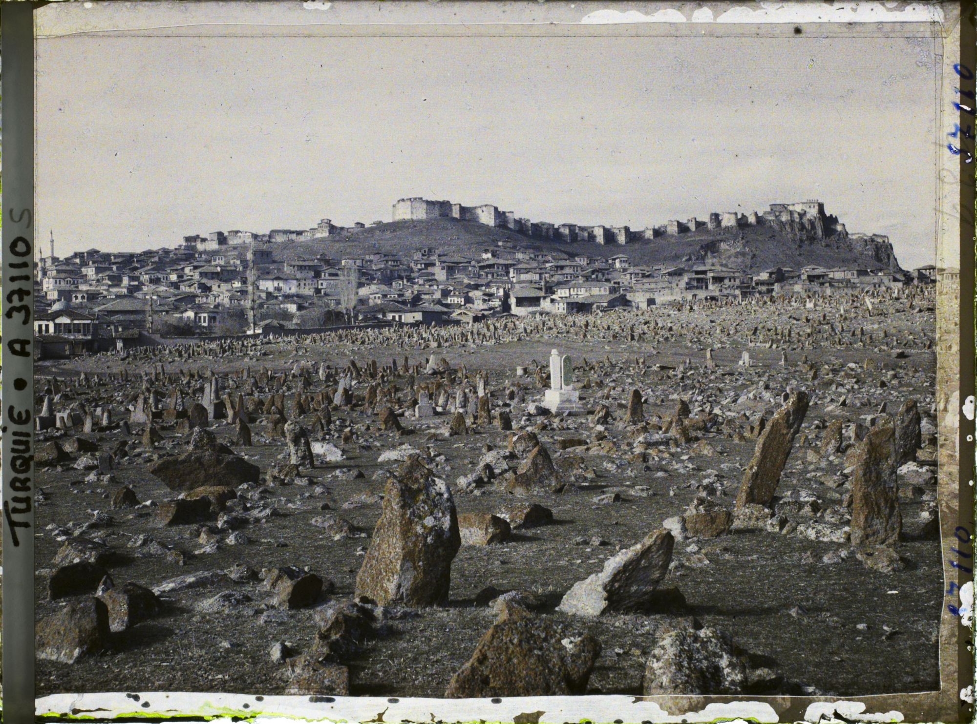 Image représentant Vers la ville surmontée de sa citadelle. Au premier plan, pierre tombale de l'un des cimetières entourant la ville
