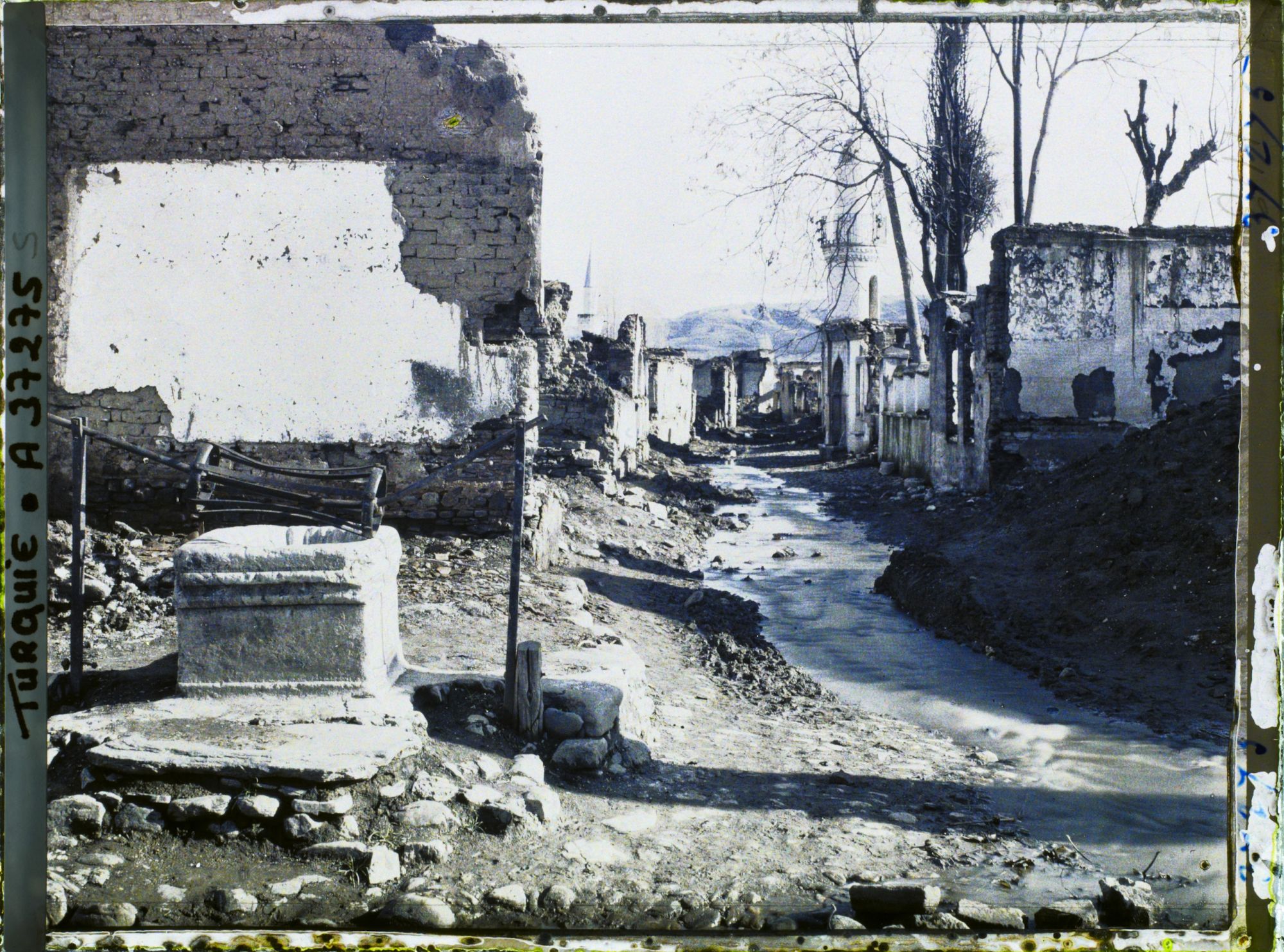 Image représentant Une rue bordée de bâtiments en ruines, dont une mosquée (quartier de Suk-Kuyu)