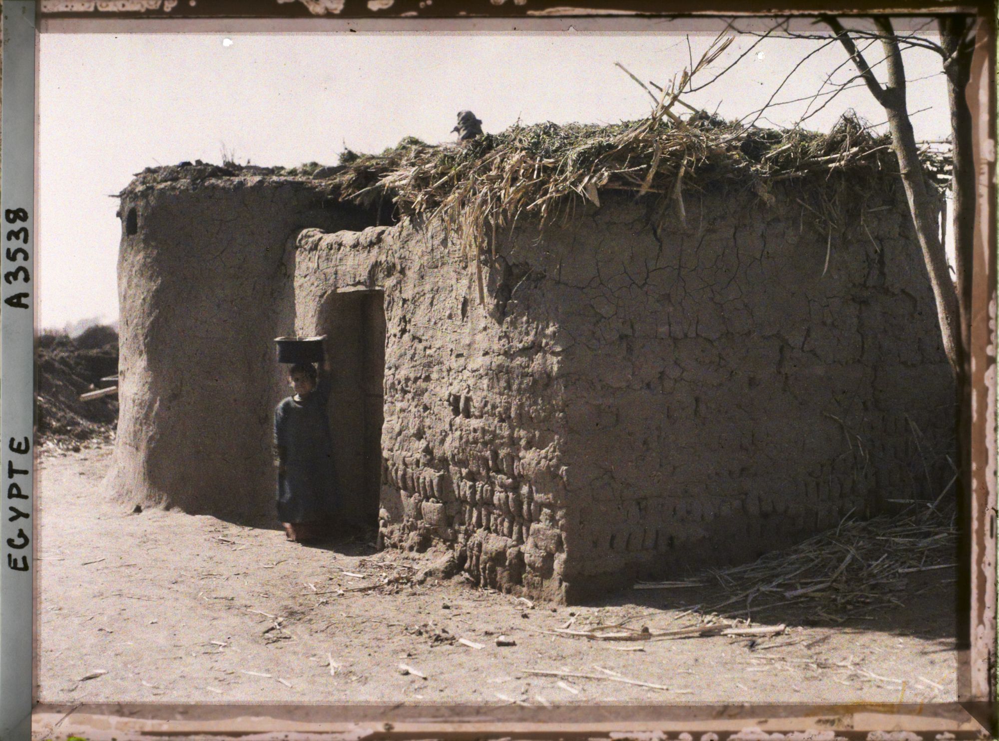 Image représentant Fillette devant une petite habitation en terre séchée aux abords de la capitale