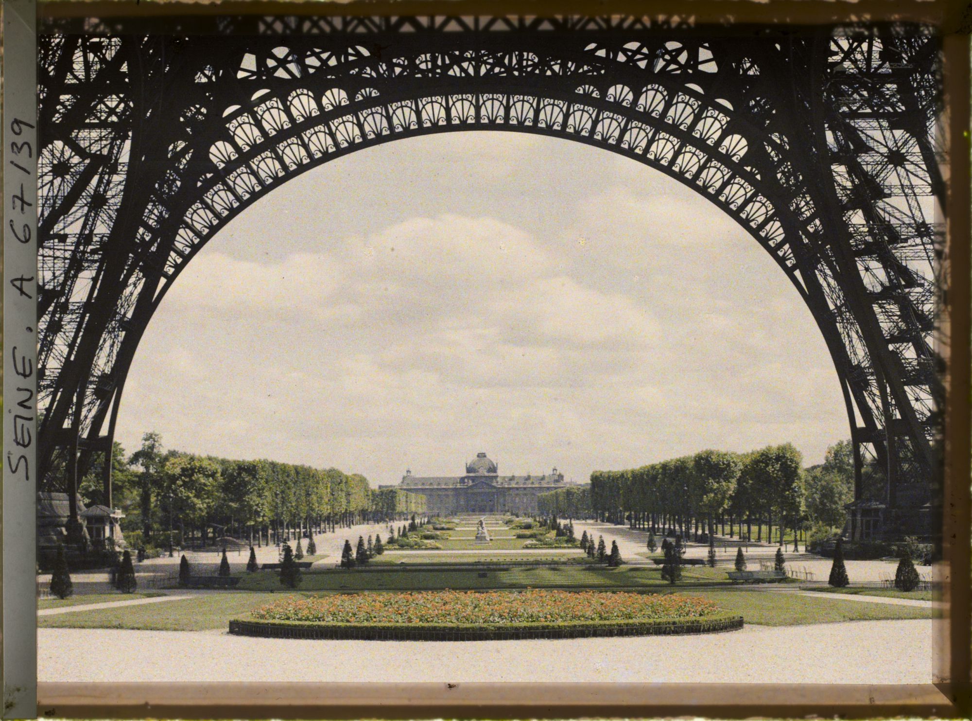 Image représentant Les jardins du Champ-de-Mars et l'Ecole militaire vus à travers les arches de la tour Eiffel