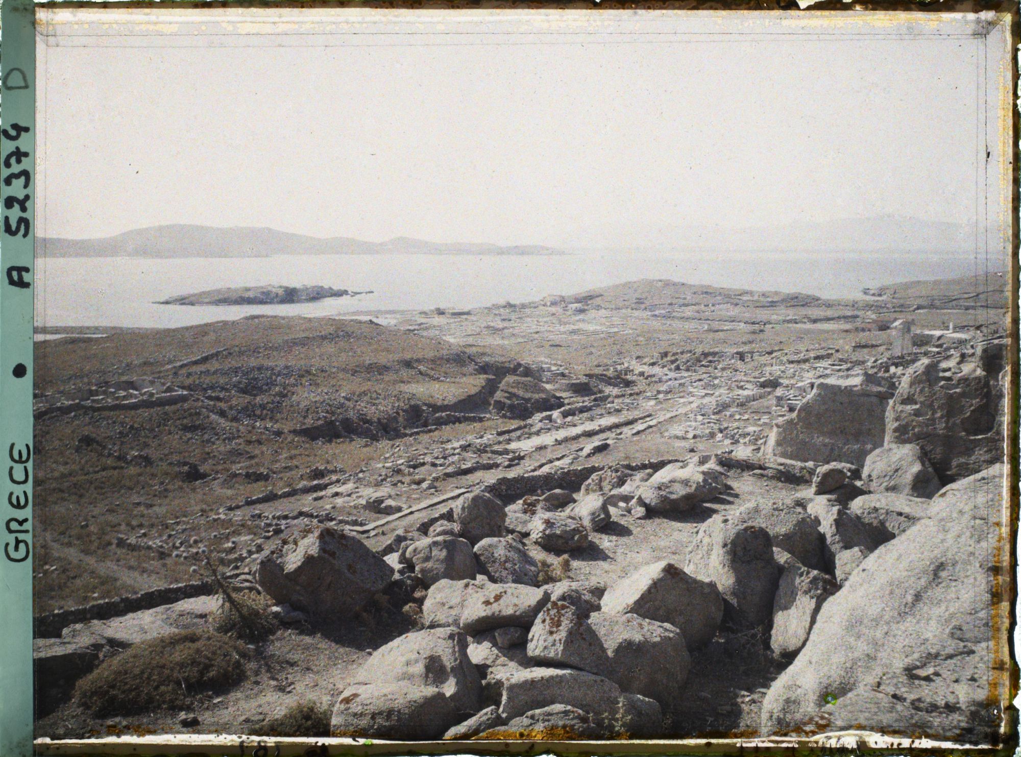Image représentant Panorama vers les ruines de la ville antique (haute et basse) et la mer, depuis l'antre du Cynthe sur le versant occidental du mont Cynthe (au fond, l'Ile de Syros)