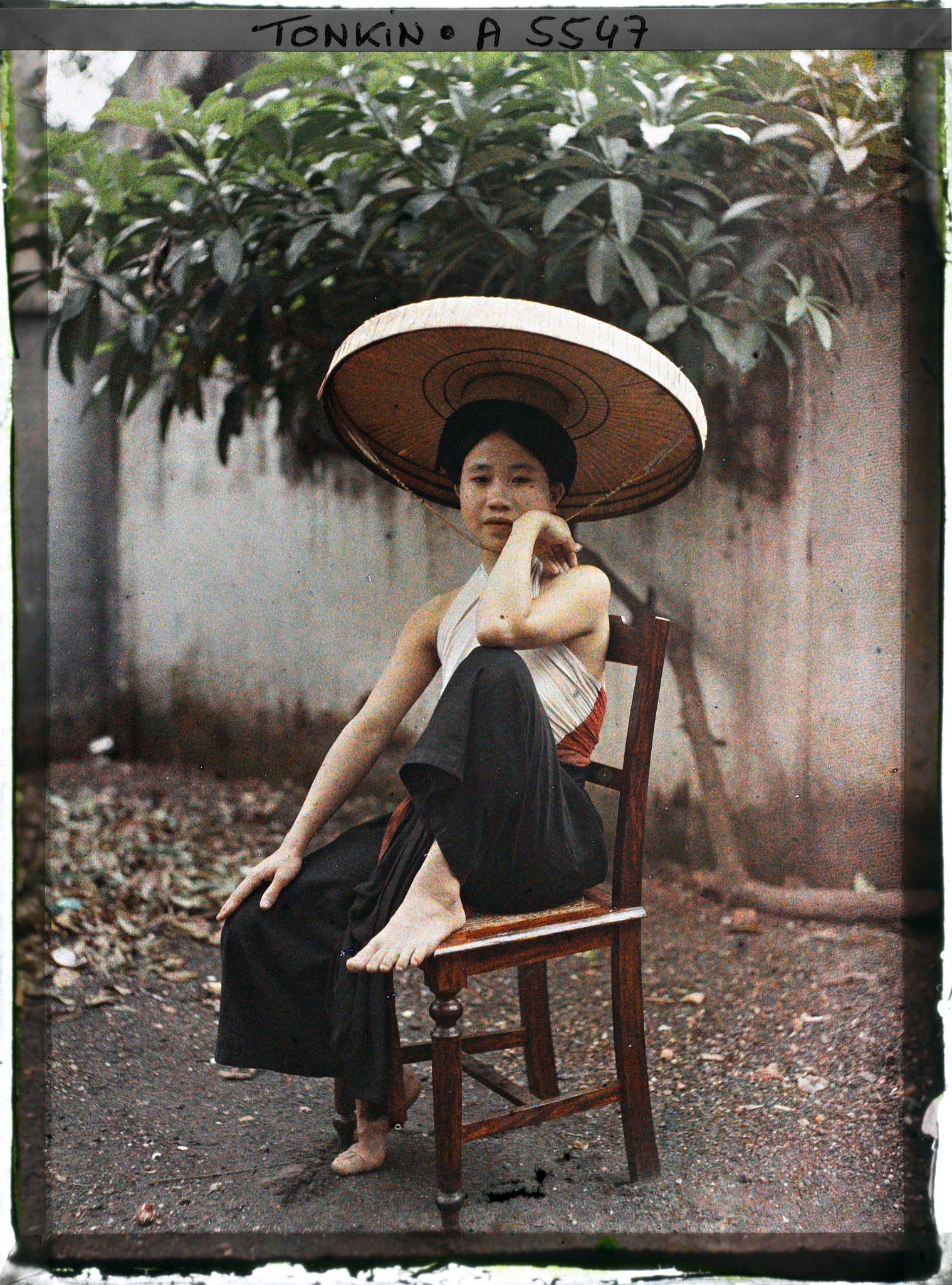 Image représentant Une jeune femme du peuple en pantalon ample et cache-sein, coiffée du grand chapeau en feuilles de latanier