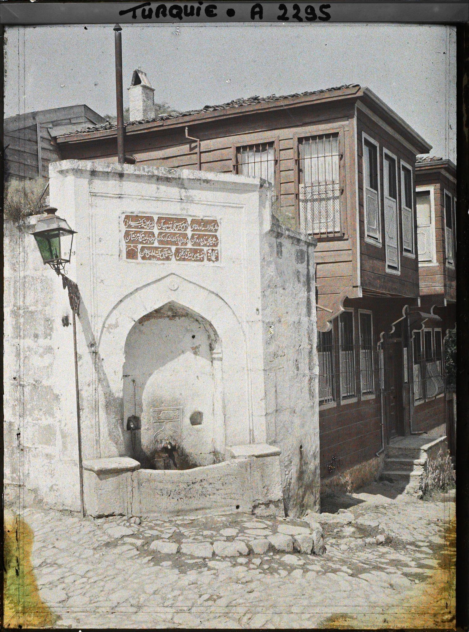 Image représentant Fontaine à l'angle d'une rue et maisons de bois