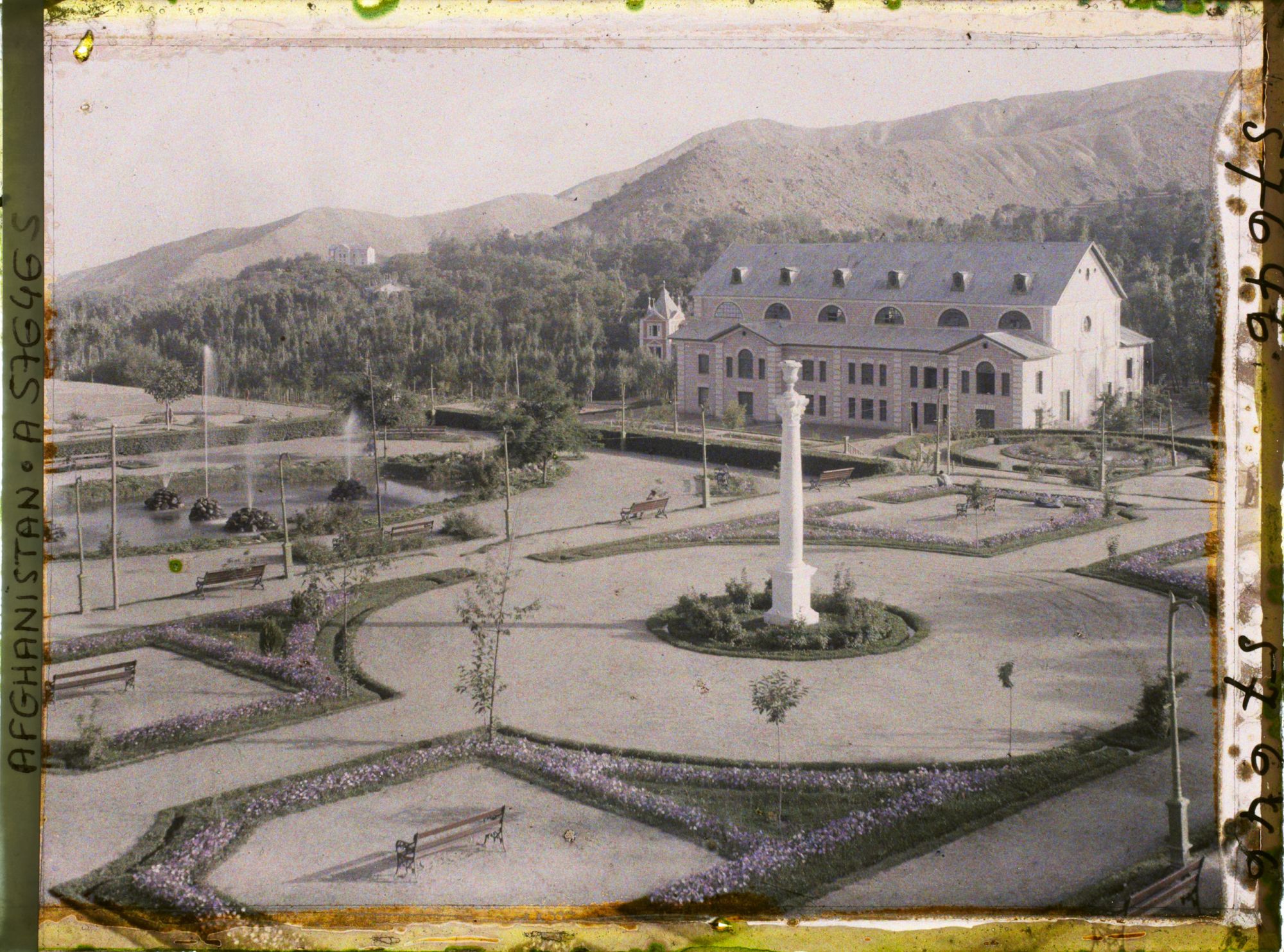 Image représentant Dans le Jardin public (Bâgh-e omumi), vue sur le jardin depuis la terrasse de la maison de thé; le bâtiment est le théâtre de Paghman (sahna-ye tamsil)