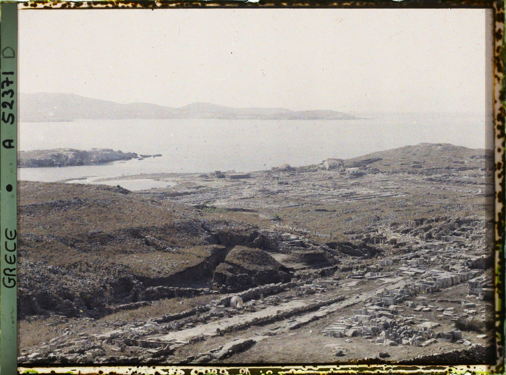 Image représentant Panorama vers les ruines de la ville antique (haute et basse) et la mer depuis l'Antre du Cinthe sur le versant occidental du mont Cinthe (au fond, l'Ile de Syros)