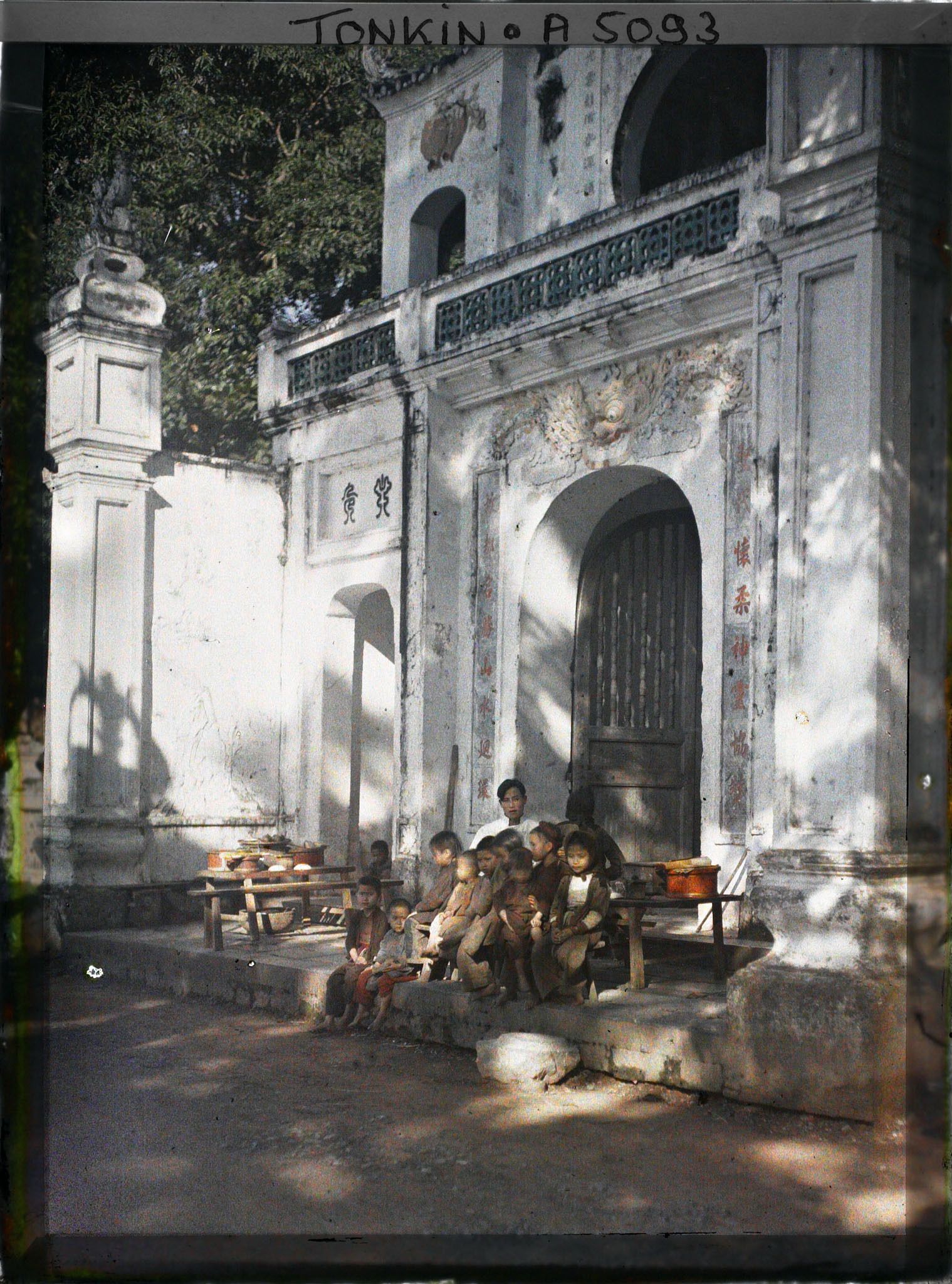 Image représentant Un homme et un groupe d'enfants assis devant le portique d'entrée du temple Chan-vu (ou Tran-vu) dans le quartier de la Citadelle (le Grand Lac)