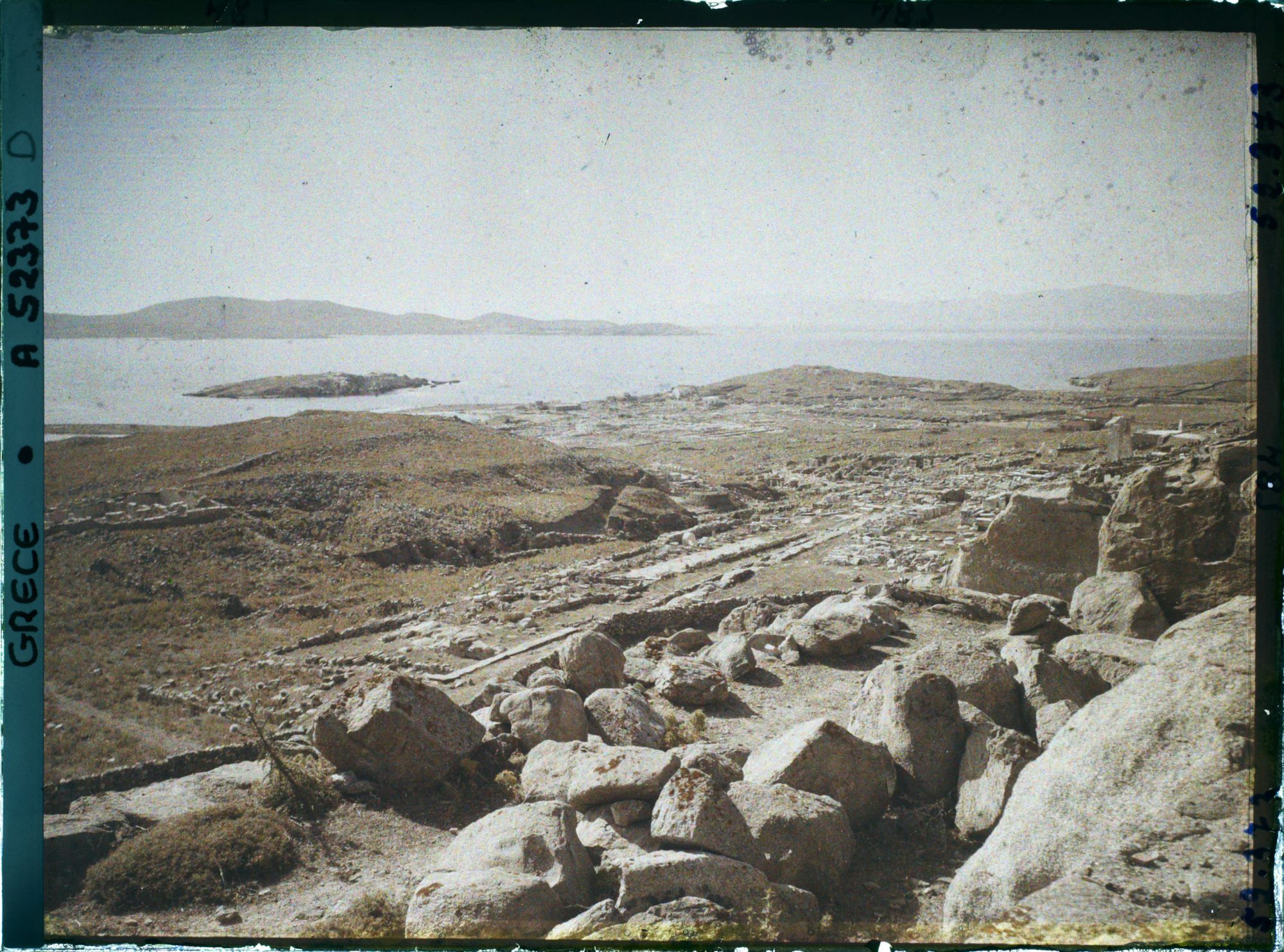 Image représentant Panorama vers les ruines de la ville antique (haute et basse) et la mer, depuis l'antre du Cynthe sur le versant occidental du mont Cynthe (au fond, l'Ile de Syros)