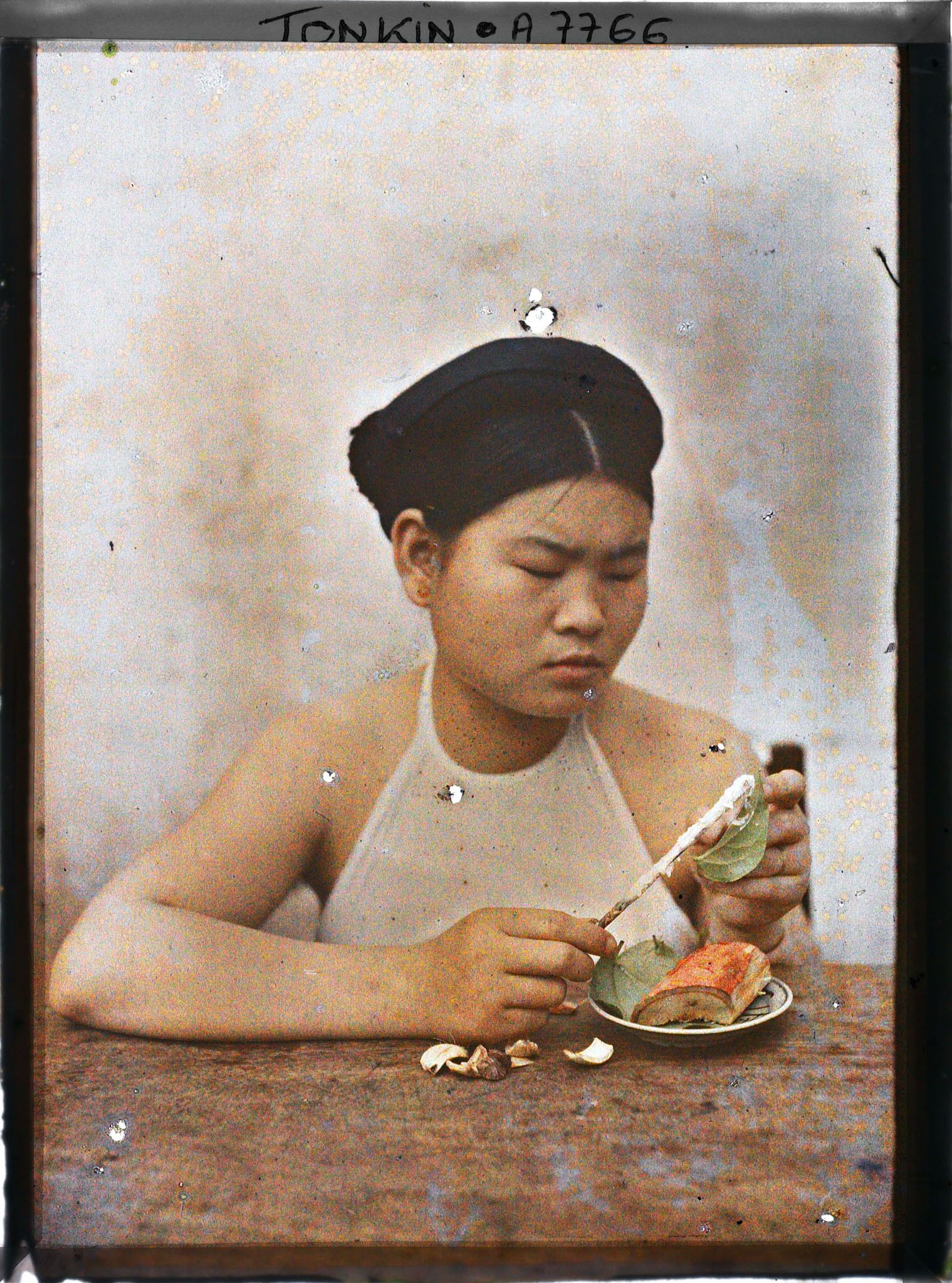 Image représentant Une jeune femme enduisant de chaux la feuille de bétel lors de la troisième phase de la confection d'une chique de bétel