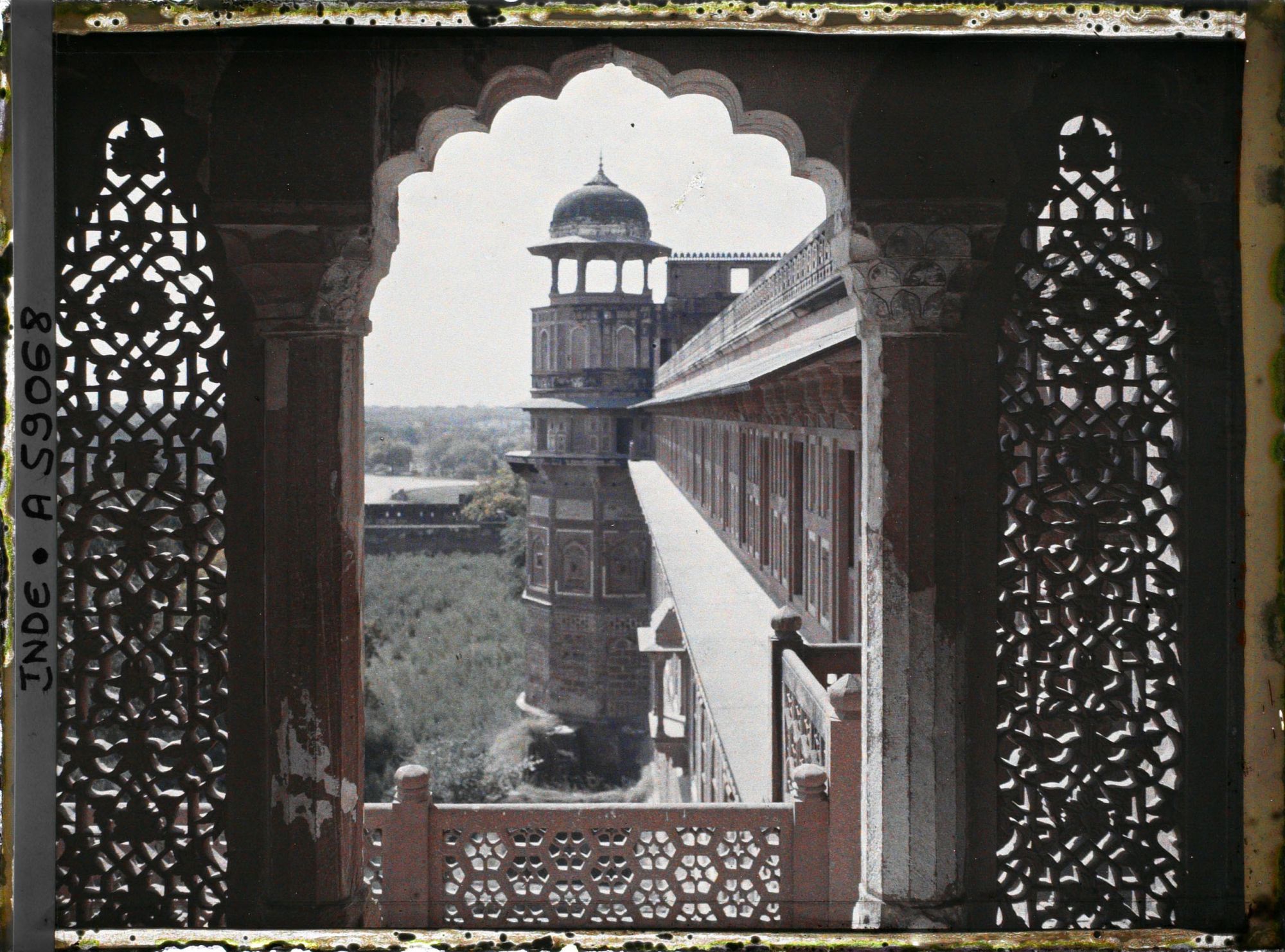 Image représentant Tour extérieure surmontée d'un chatri, vue d'une fenêtre encadrée de jalis (dentelle de pierre formant claustra) dans le fort Rouge (Lal Qila)