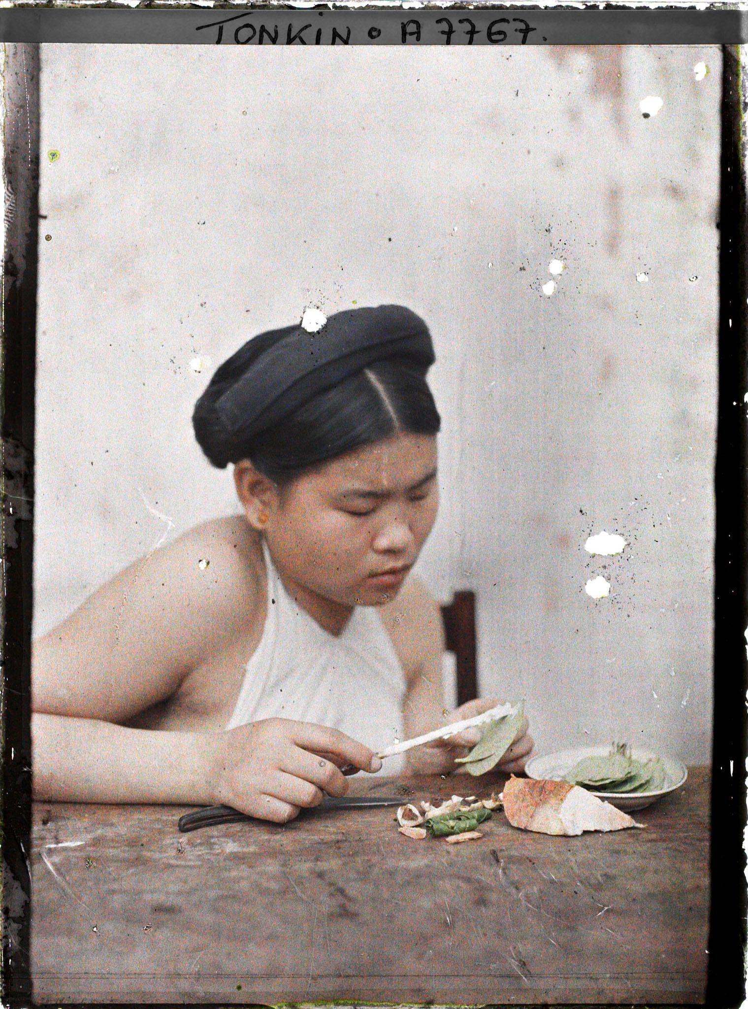 Image représentant Une jeune femme enduisant de chaux la feuille de bétel lors de la troisième phase de la confection d'une chique de bétel