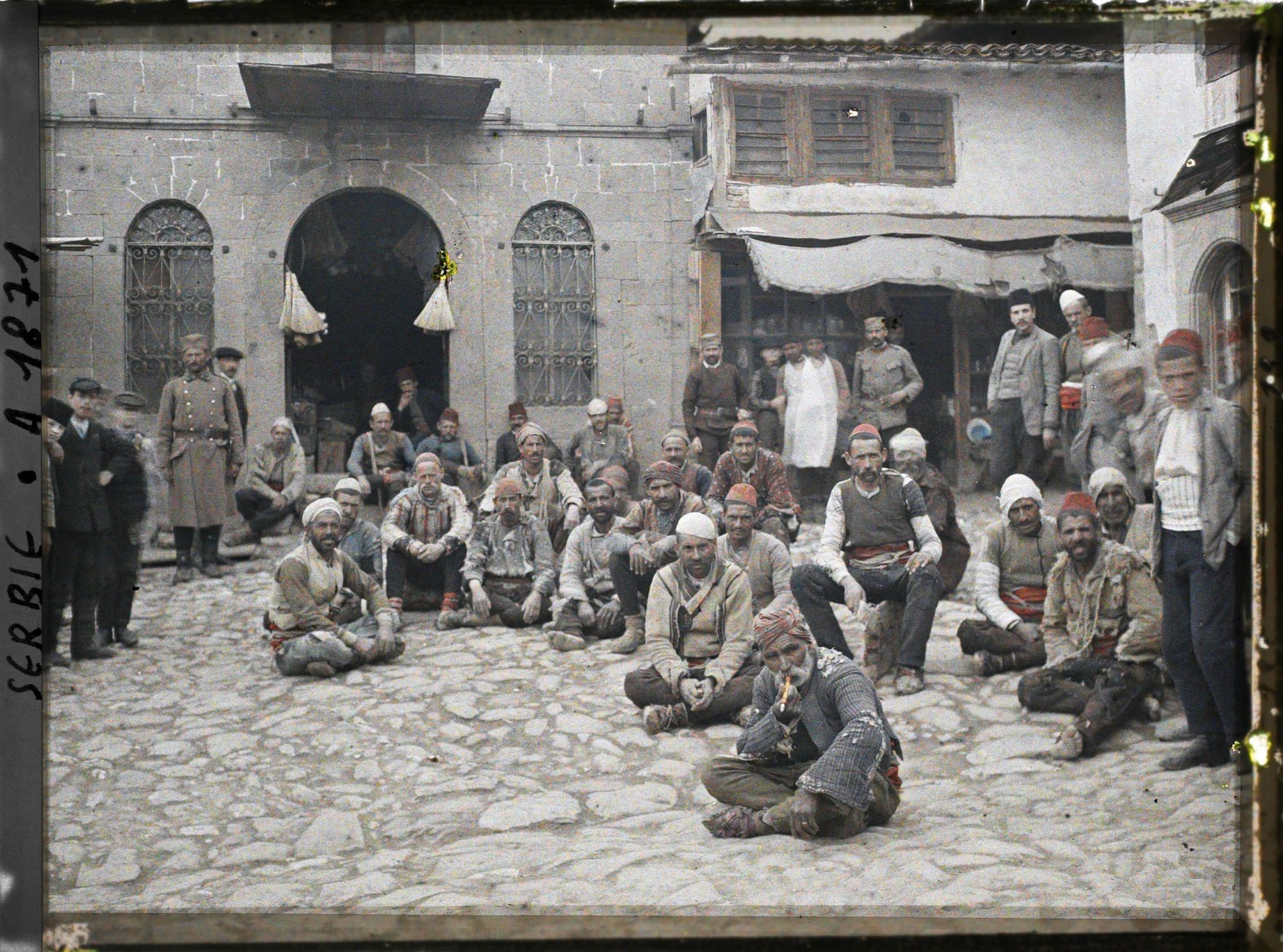 Image représentant Groupe de portefaix tziganes assis devant d'autres habitants et soldats
