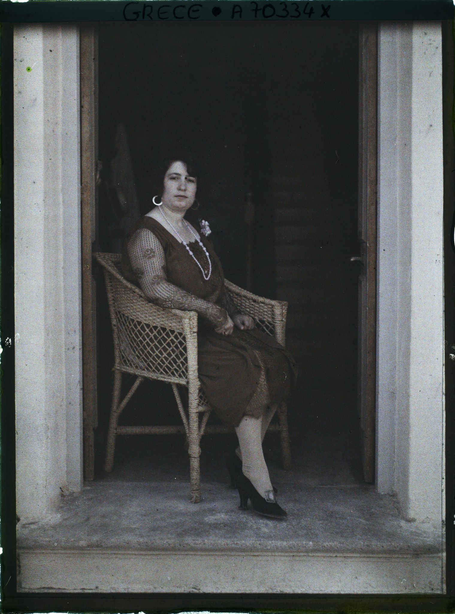 Image représentant Femme d'une quarantaine d'années élégamment vêtue, assise sur seuil d'une maison ou d'un hôtel (guide, interprète, compagne de l'opérateur ?)