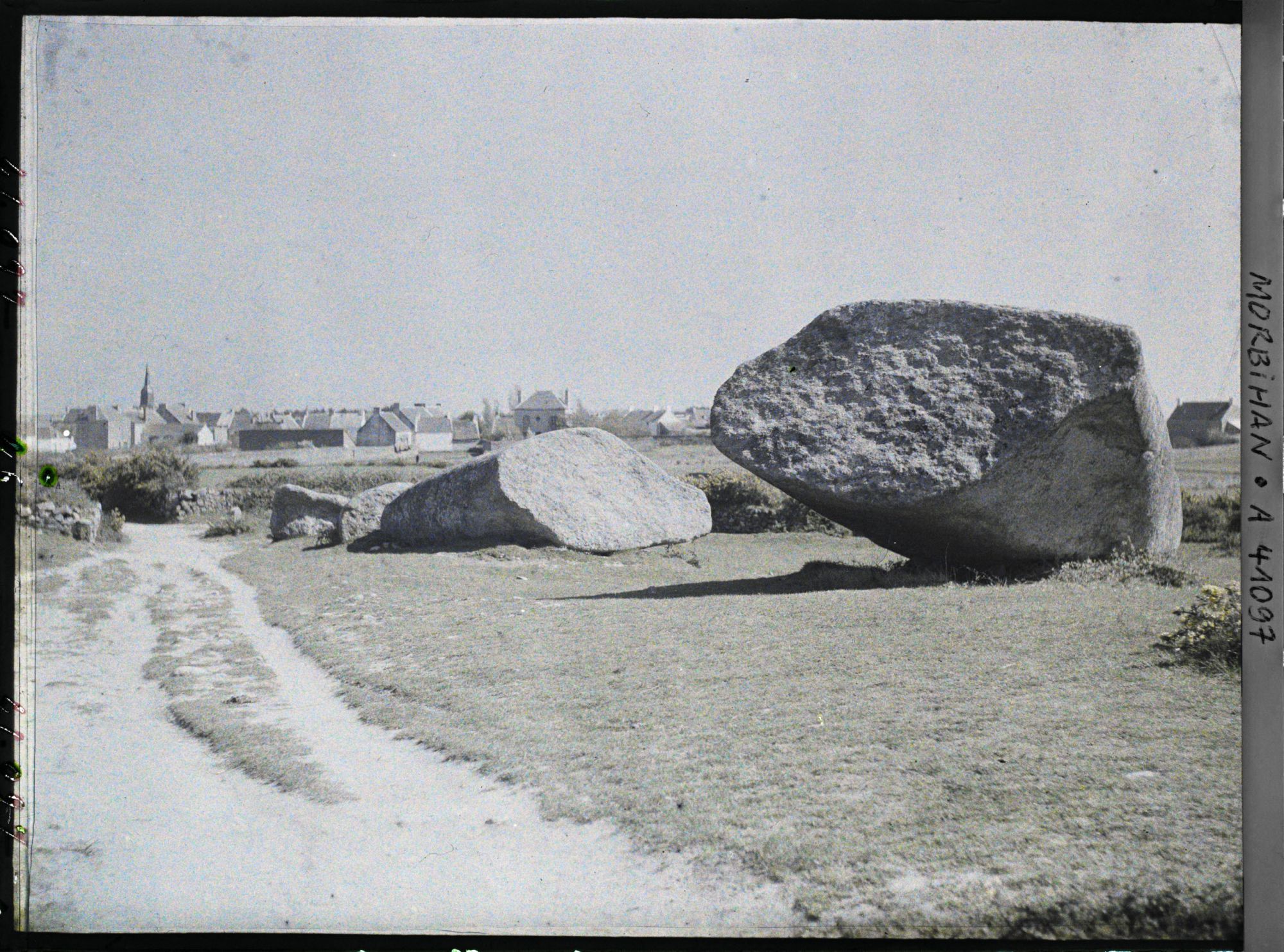 Image représentant Le Grand Menhir brisé ; à l'arrière-plan, le village de Locmariaquer