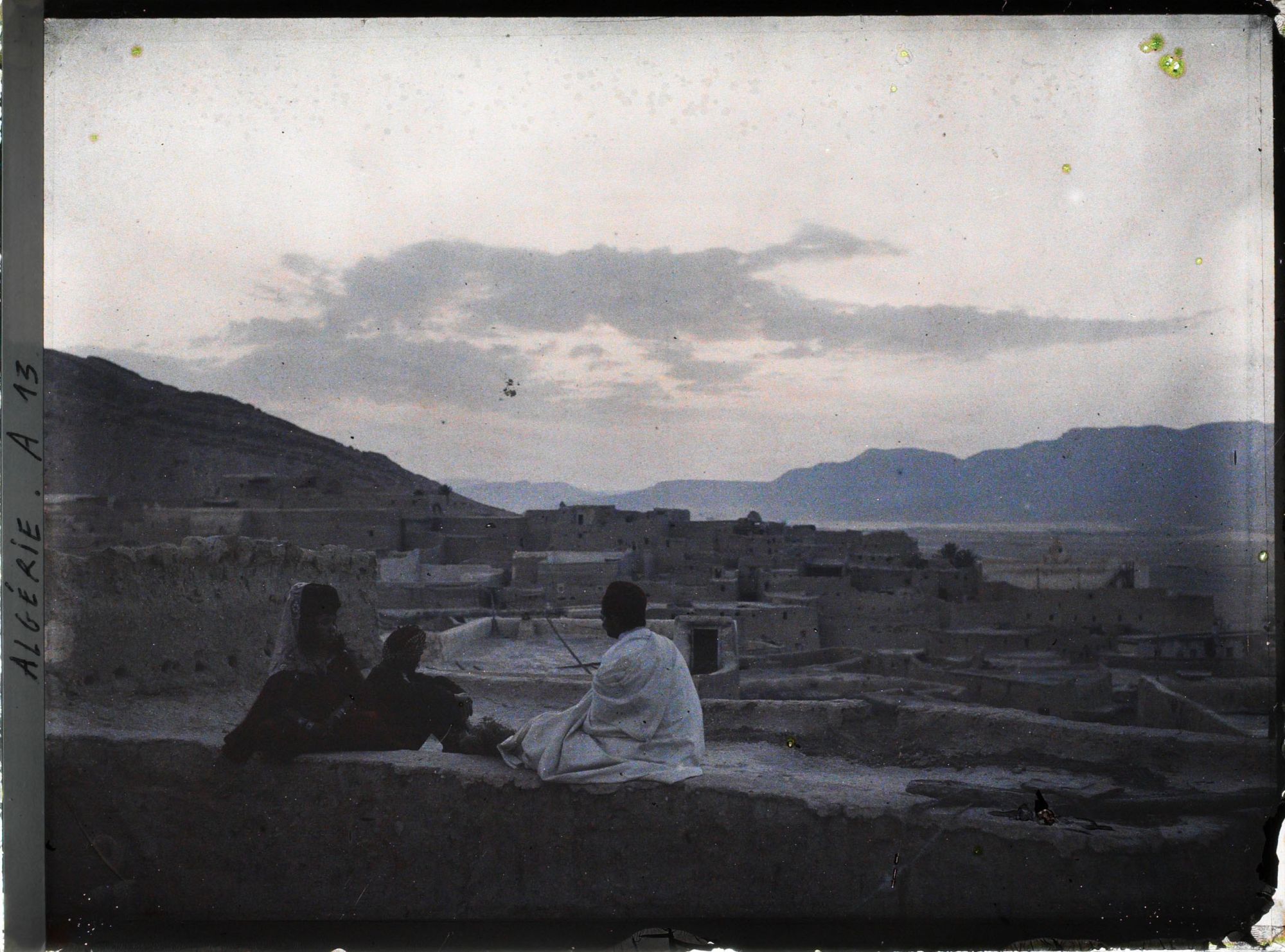 Image représentant Panorama sur la ville avec trois personnes assises sur le bord d'une terrasse, vers le soir