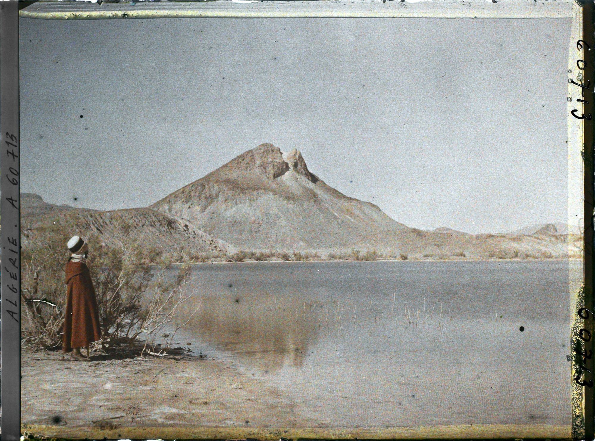 Image représentant Un homme se tient sur la rive du lac ; à l'arrière-plan, les pitons de marne verte