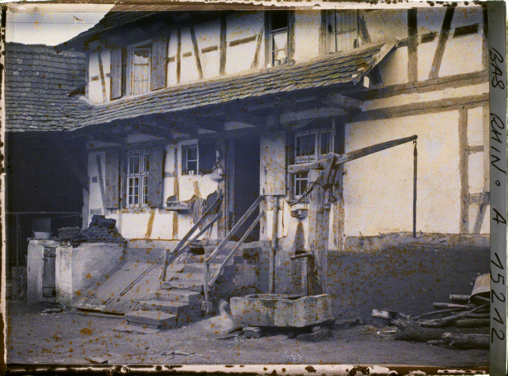 Image représentant France Alsace, Strasbourg, Langolsheim : un type de grande ferme rurale de la Campagne Strasbourgeoise l'entrée de la maison du maître, l'escalier, la pompe du puits et la Cave.