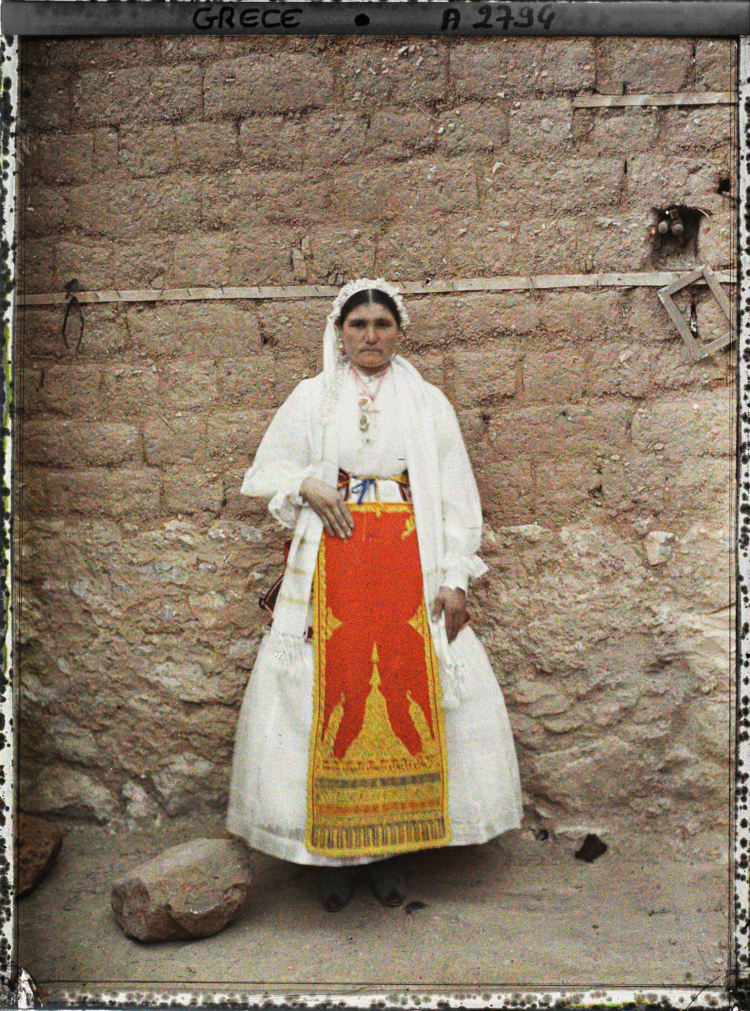 Image représentant Une villageoise en costume de cérémonie (robe blanche et tablier rouge bordée or)