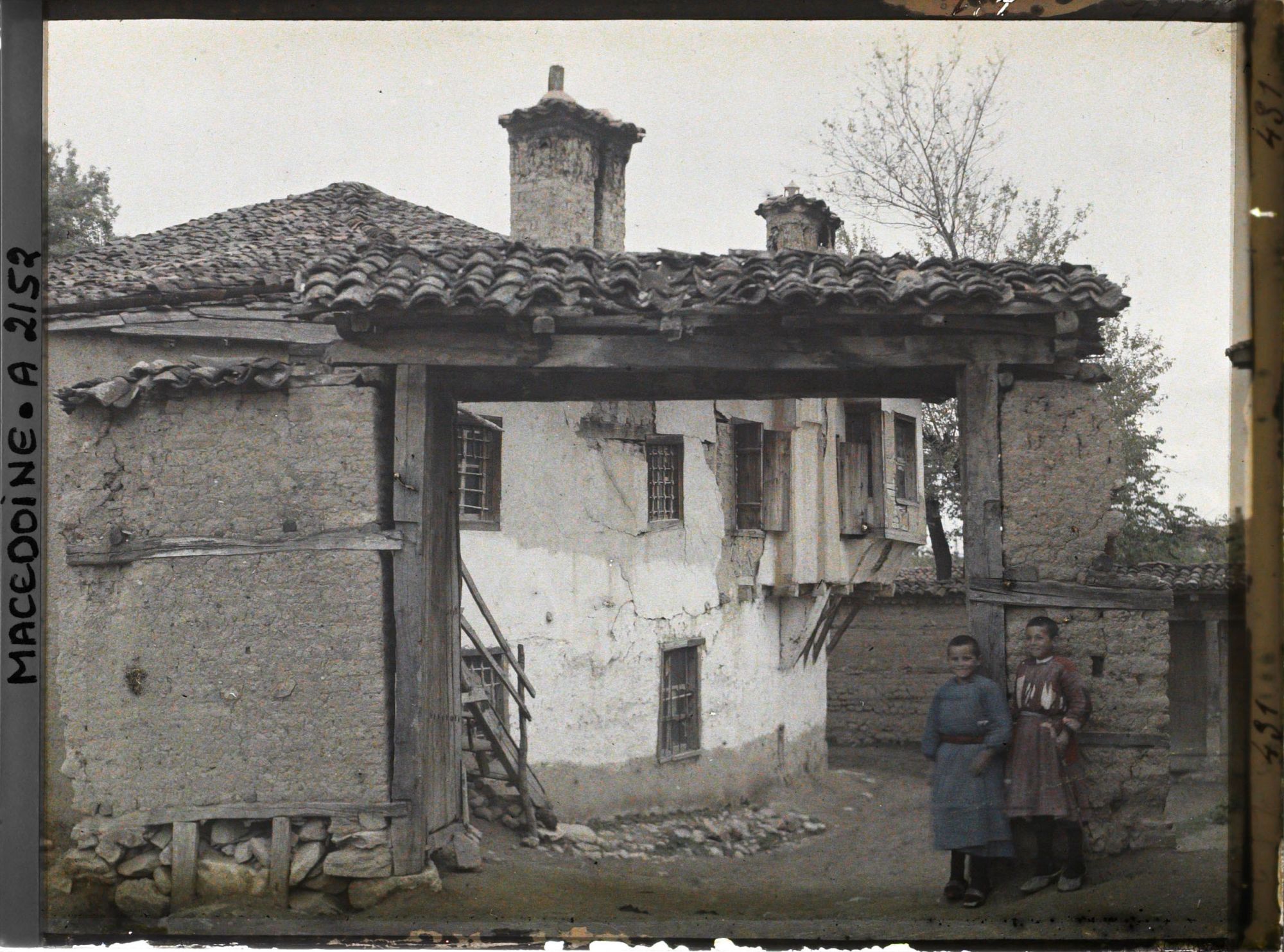 Image représentant Maison à travers une porte de bois s'appuyant sur des montants de brique crue avec deux enfants