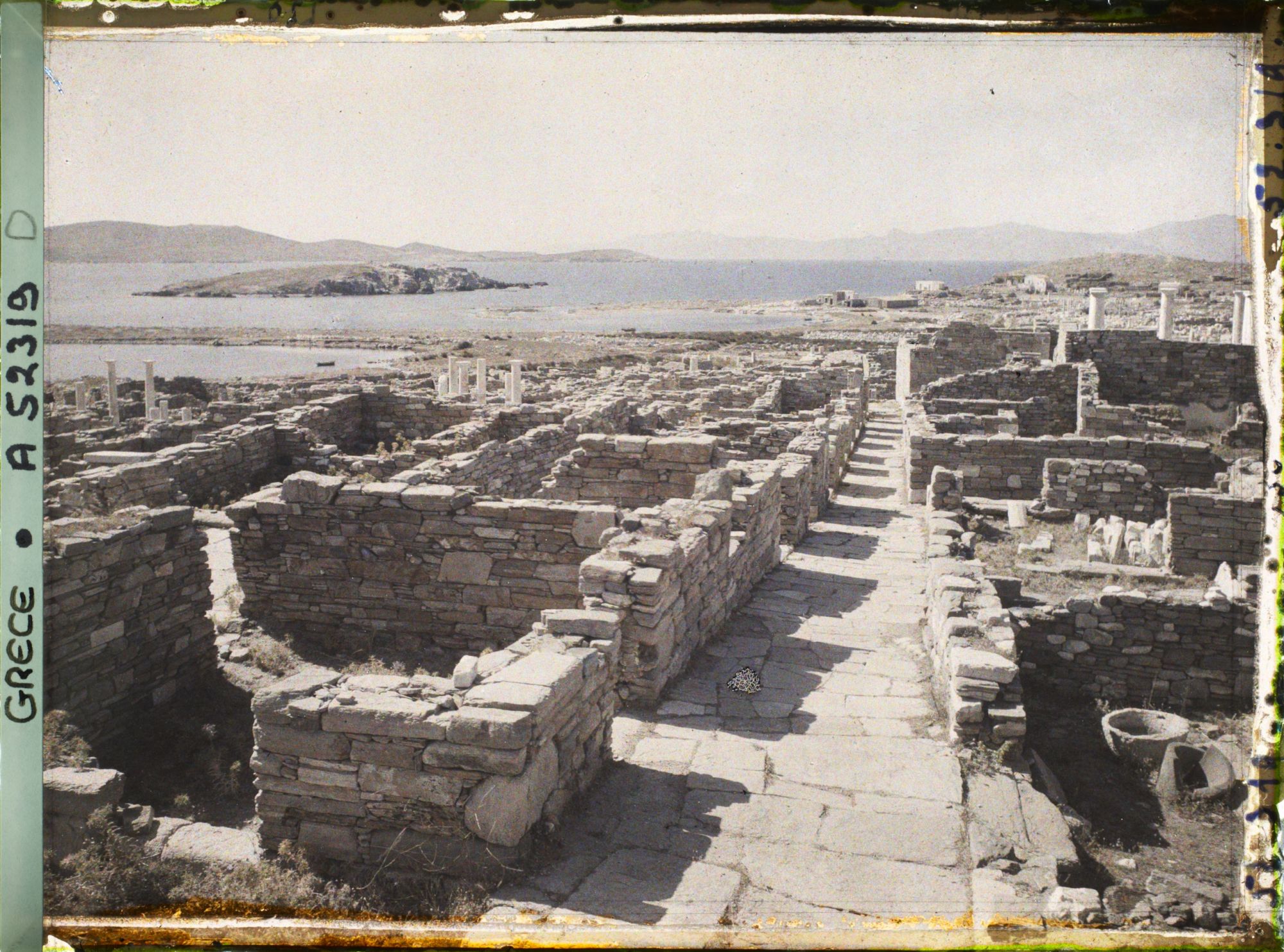Image représentant La rue du Théâtre, vue vers la ville basse. Au fond, l'ile de Tinos