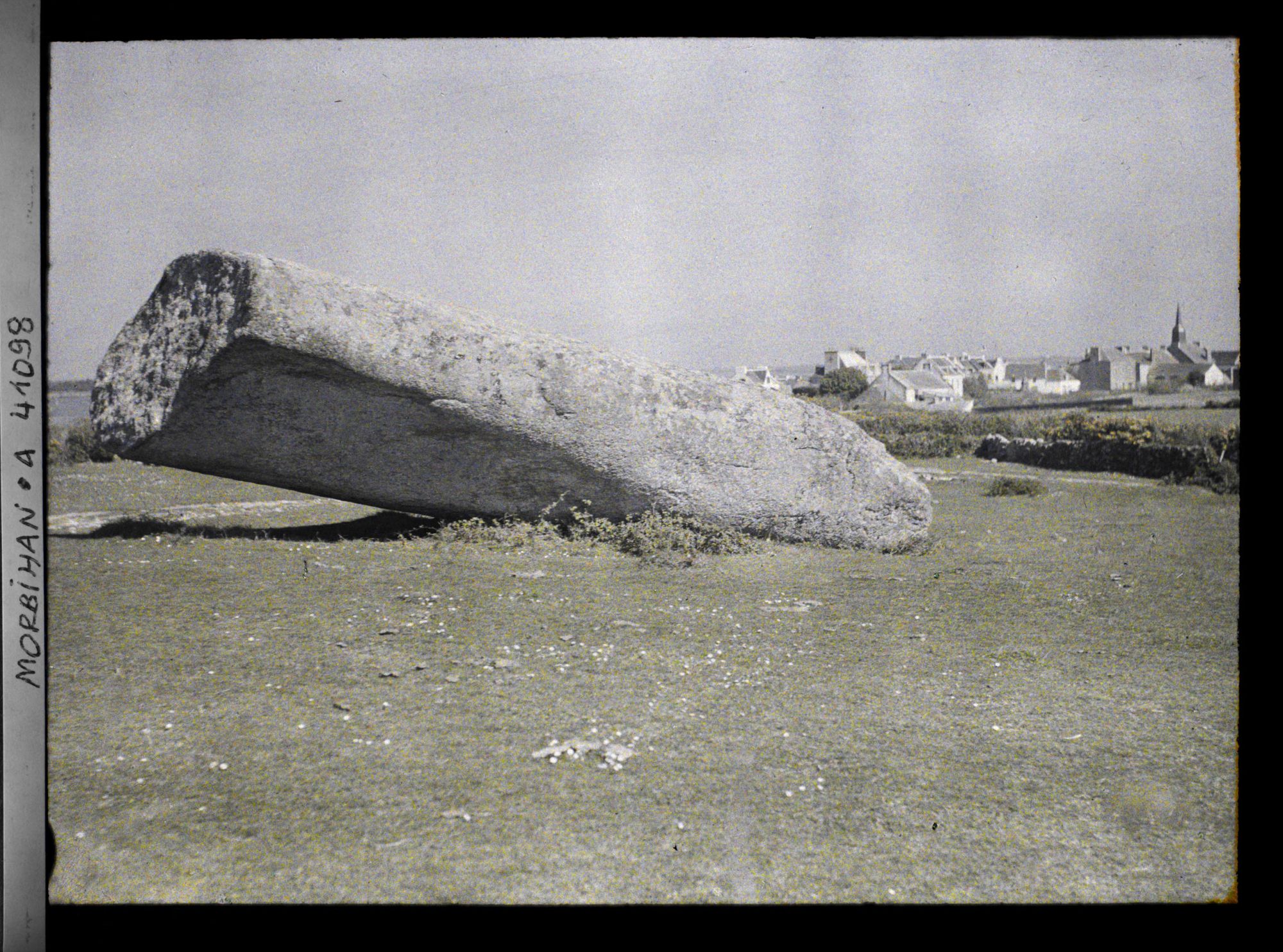 Image représentant Le plus gros des quatre fragments du Grand Menhir brisé ; à l'arrière-plan, le village de Locmariaquer