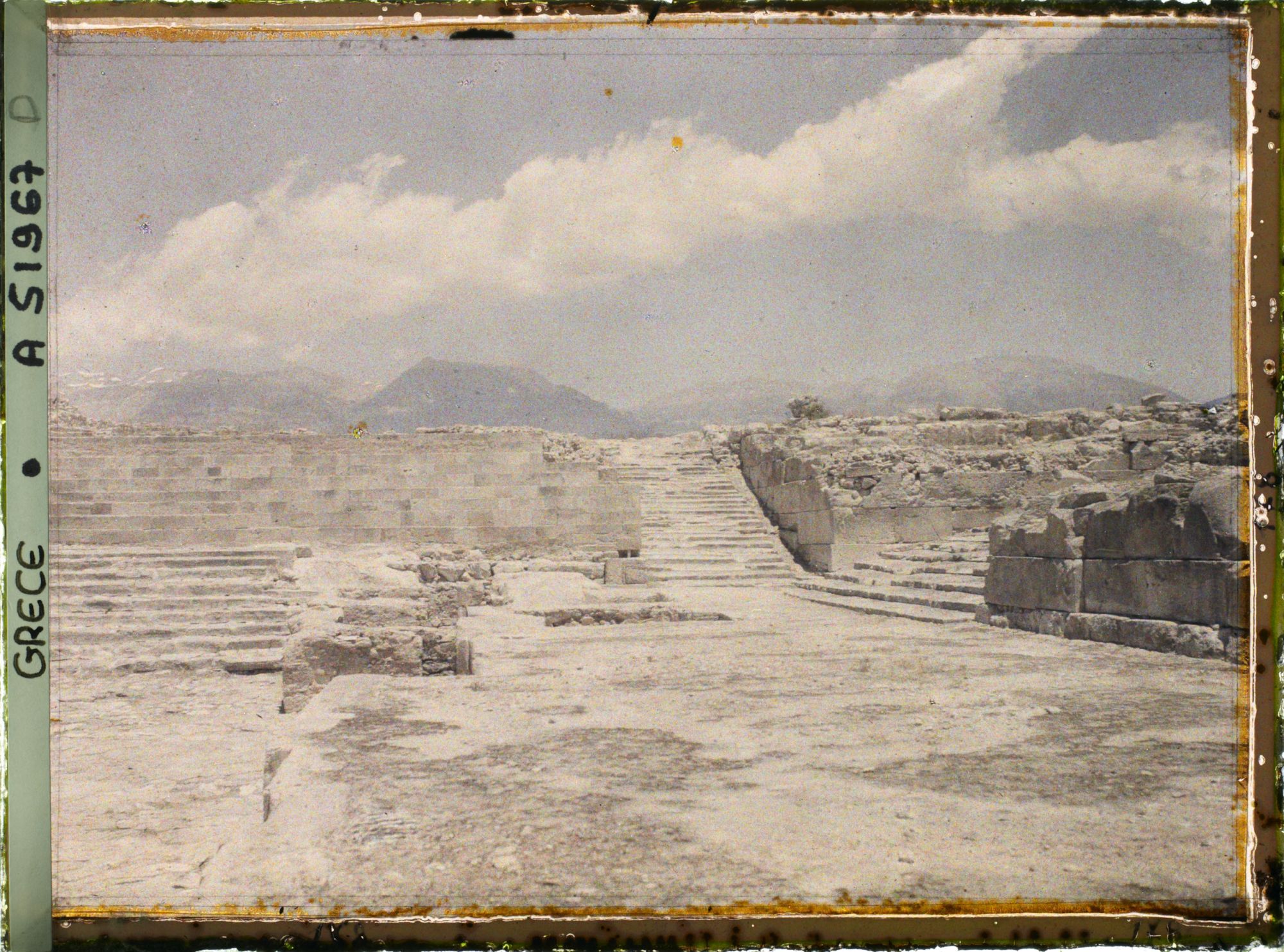 Image représentant Le palais dans la cour occidentale, les gradins d'un théâtre. Au centre, l'escalier nord. A droite, le grand escalier (menant aux grands Propylées)
