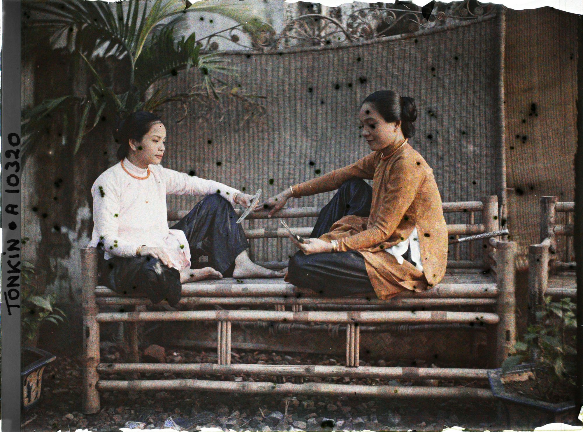 Image représentant Deux jeunes femmes saïgonnaises de classe aisée, jouant aux cartes assises sur une banquette en bambou