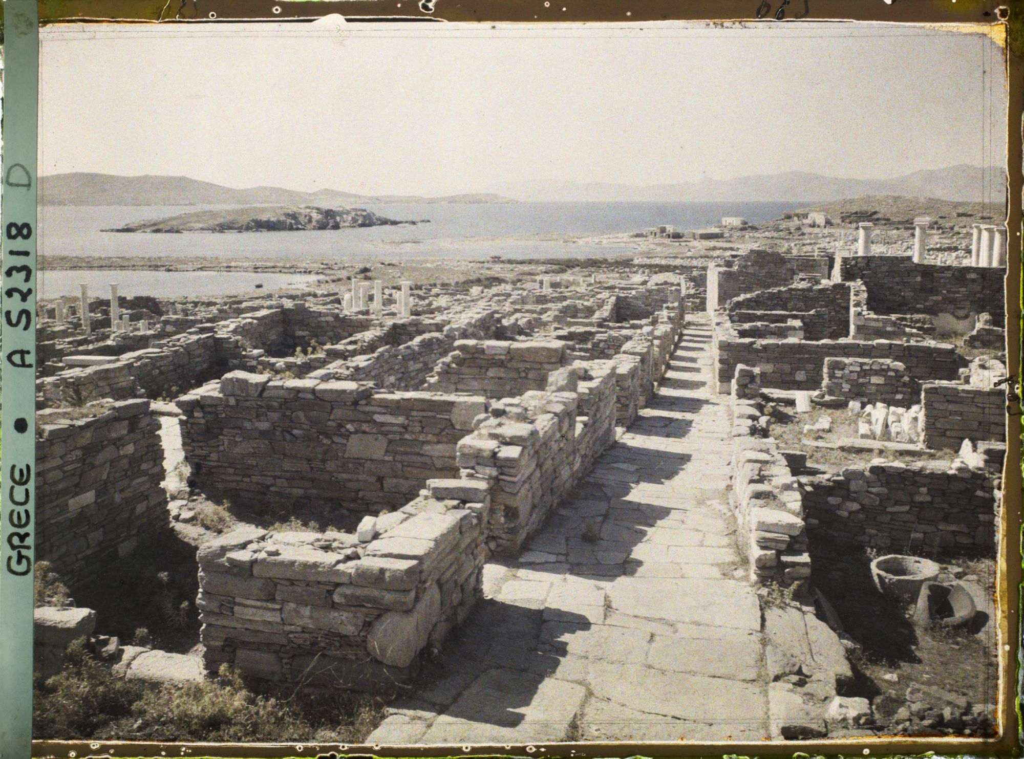 Image représentant La rue du Théâtre, vue vers la ville basse. Au fond, l'ile de Tinos