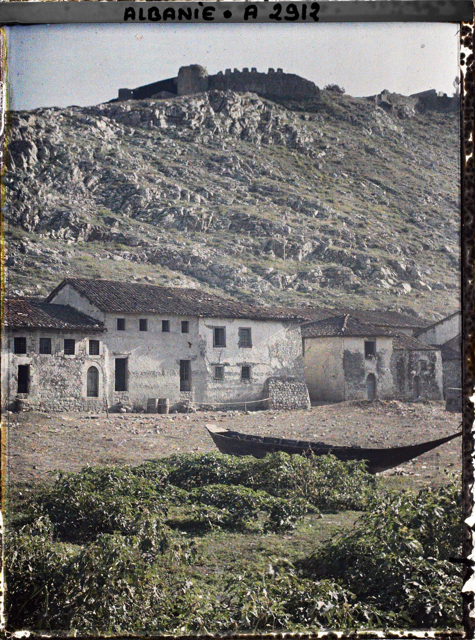 Image représentant Au pied de la forteresse Rozafa, maisons du bazar et barque pirogue au bord du fleuve Buna