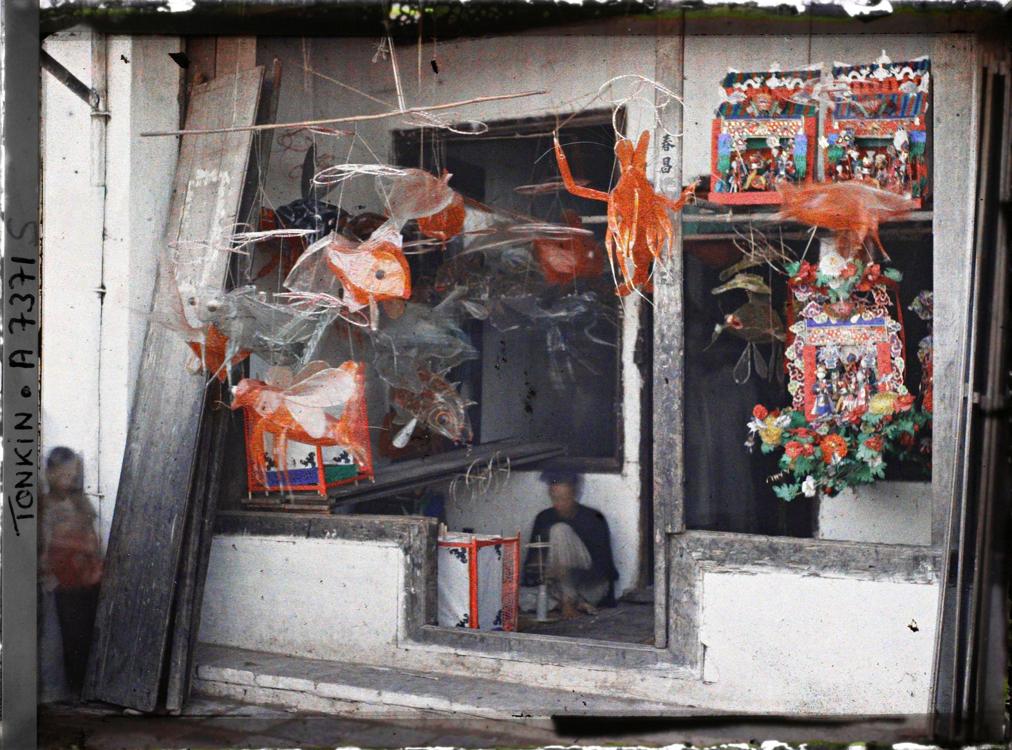 Image représentant Un étalage de jouets en papier huilé devant une boutique, dans la " rue du Chanvre "