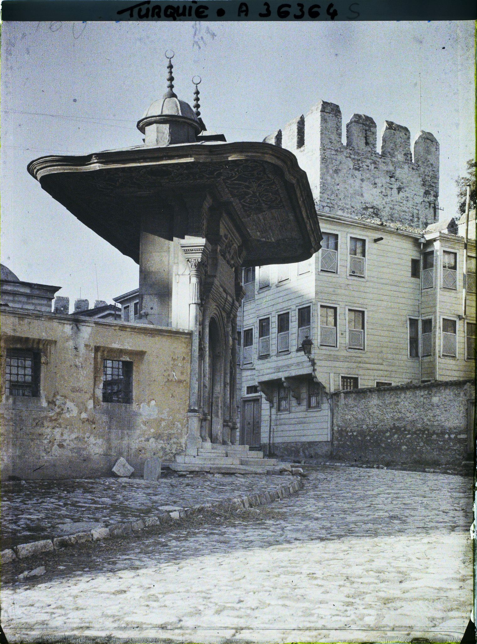 Image représentant Porte (dite du Sultan ?) d'accès à la cour du han de la Aya Sophia Camii ("mosquée Sainte-Sophie") avec à droite, la rue Sogukçesme Sokagi ("rue de la Fontaine-Froide") et une maison traditionnelle en bois (konak) adossée au mur d'enceinte du palais de Topkapi