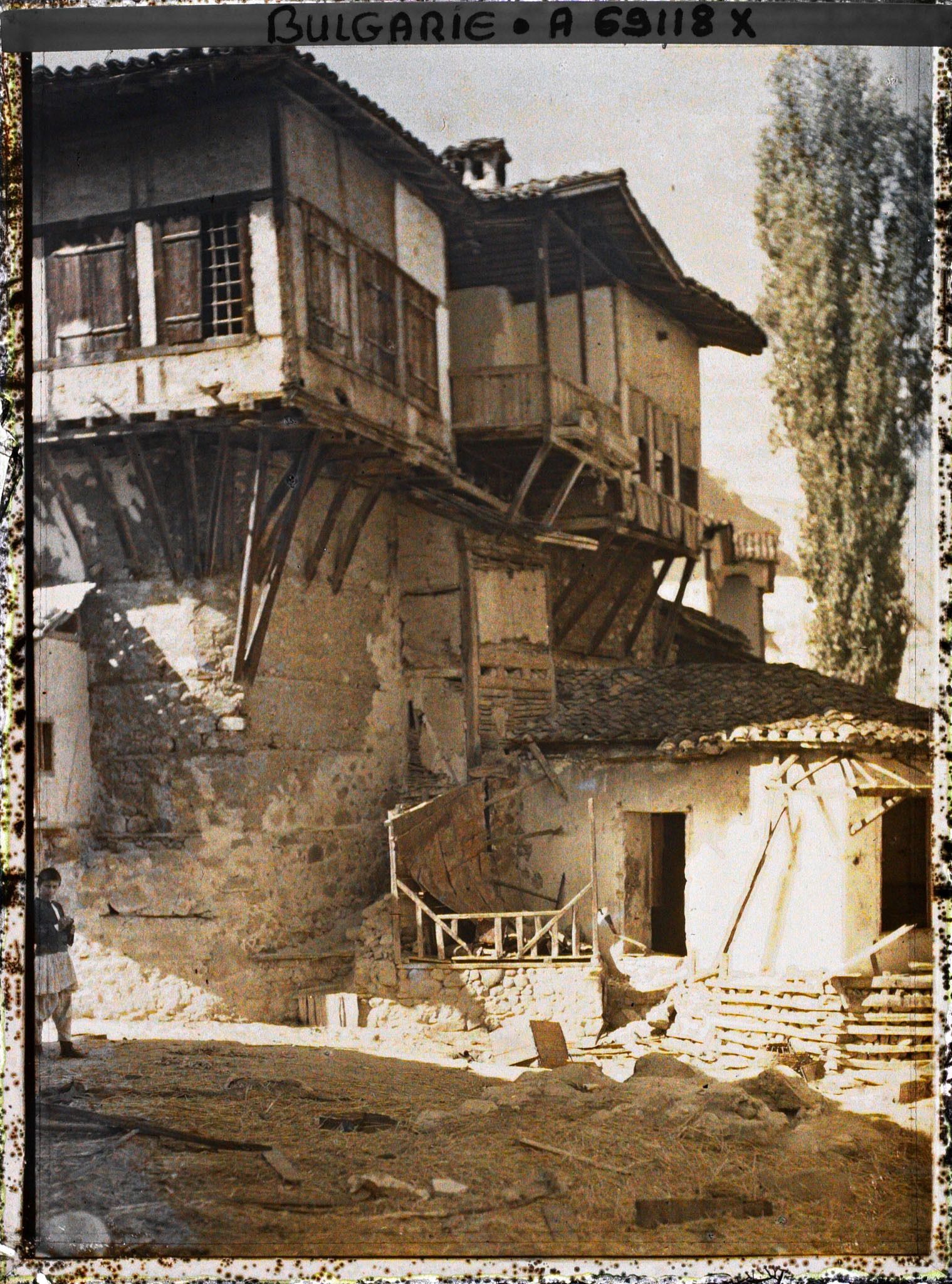 Image représentant Rue de terre battue jonchée de paille ou cailloux, morceaux de bois et maisons en étages